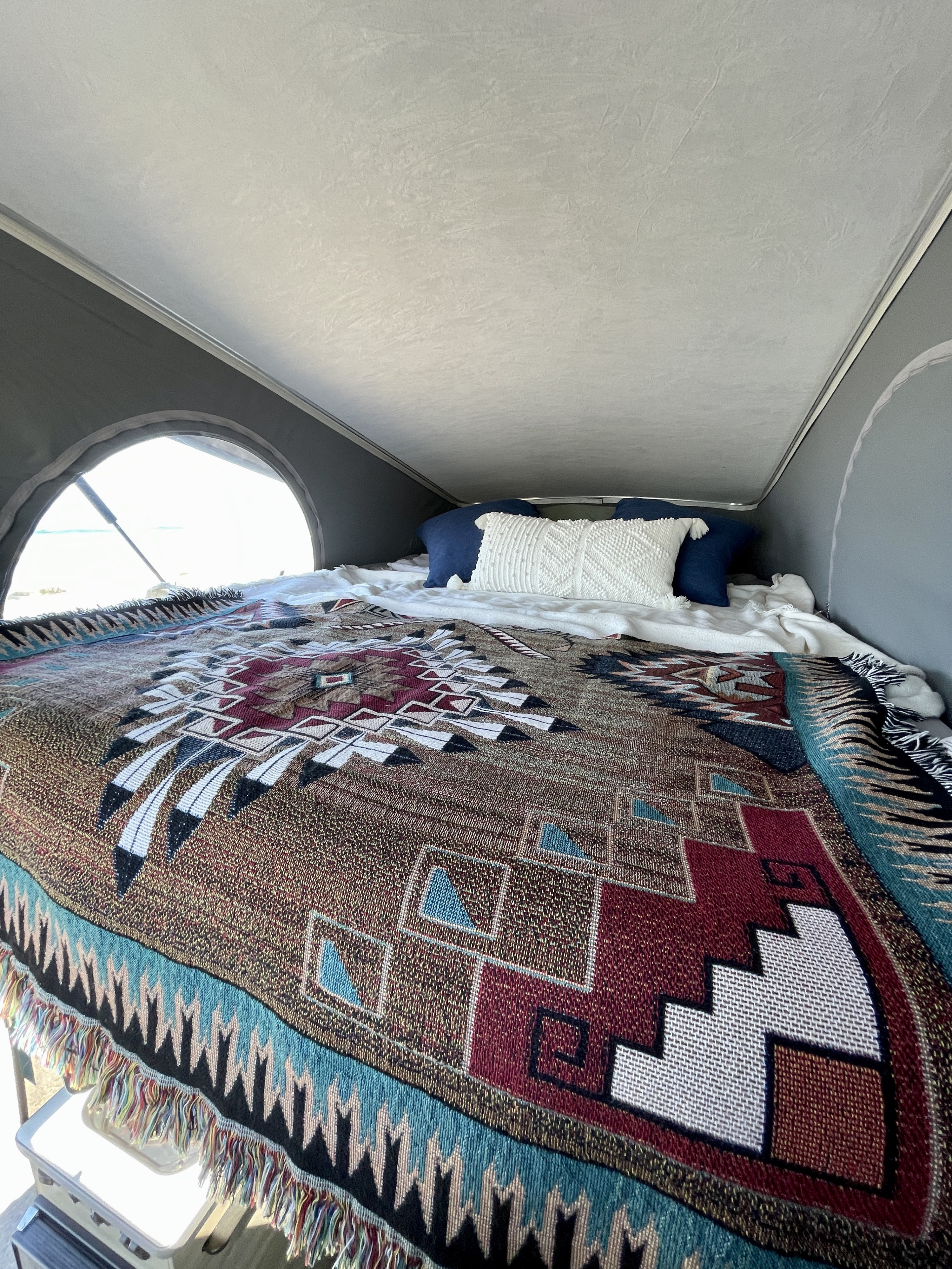 Cozy sleeping area in an RV rental, featuring a vibrant Southwestern blanket and pillows, with a bright window view of the outdoors.. Winnebago Solis 2021