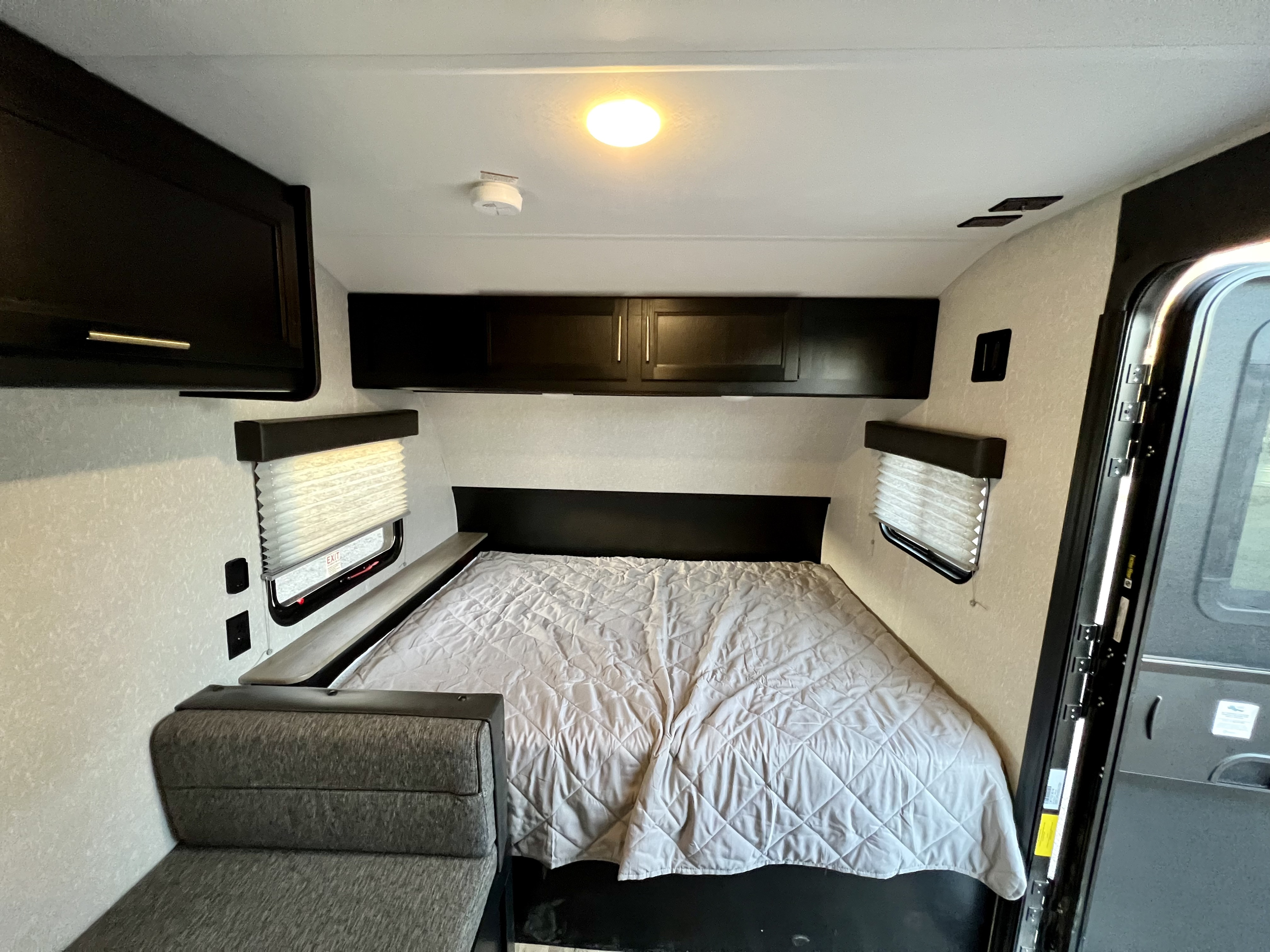 Inside an RV rental: a comfortable bedroom area with a bed, overhead cabinets, window blinds, and a smoke detector.. Forest River Cherokee Wolf Pup 2022
