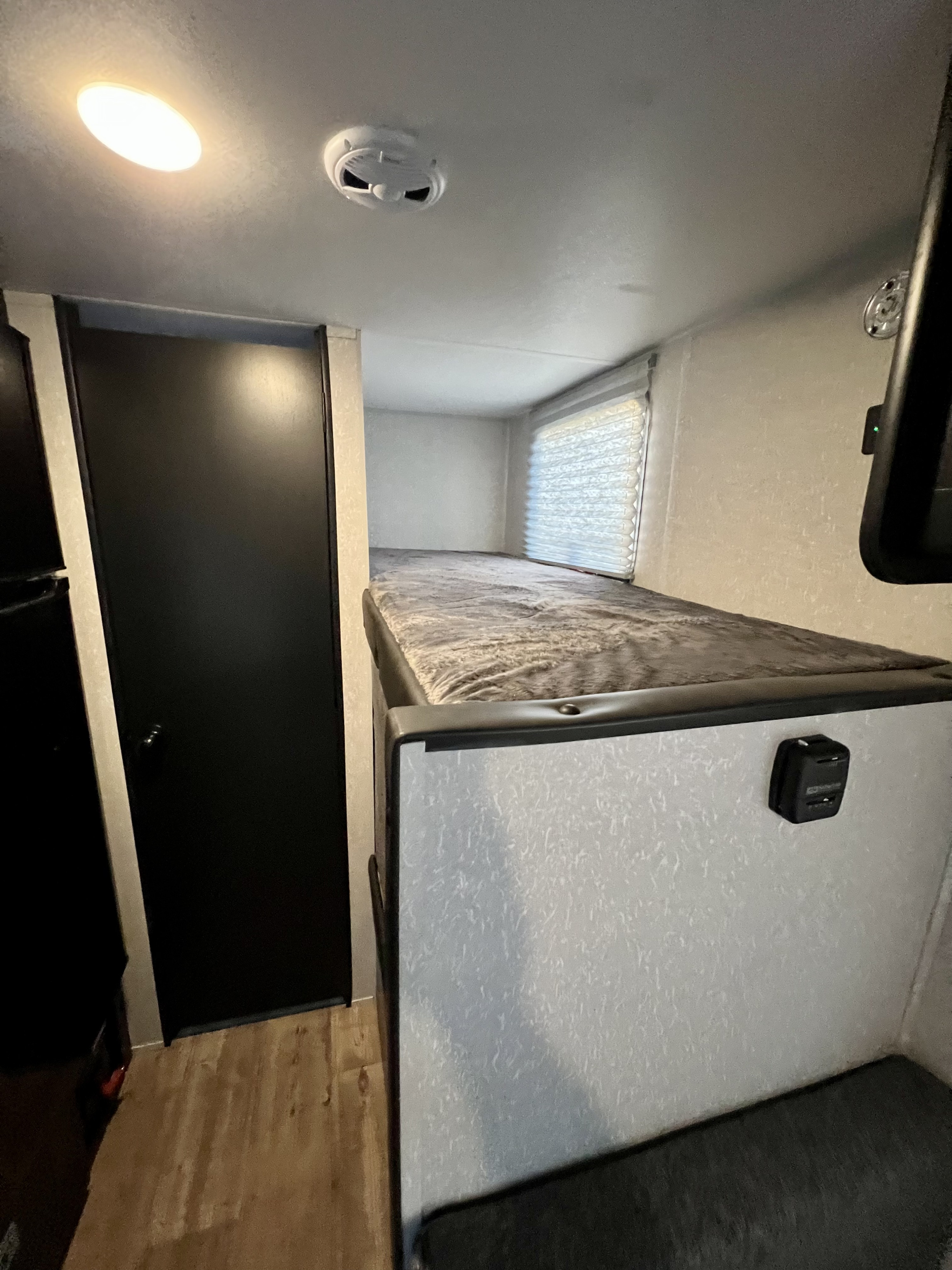 RV rental interior: bunk bed with charging port, window blinds, black door, and ceiling light. Ideal compact sleeping space.. Forest River Cherokee Wolf Pup 2022