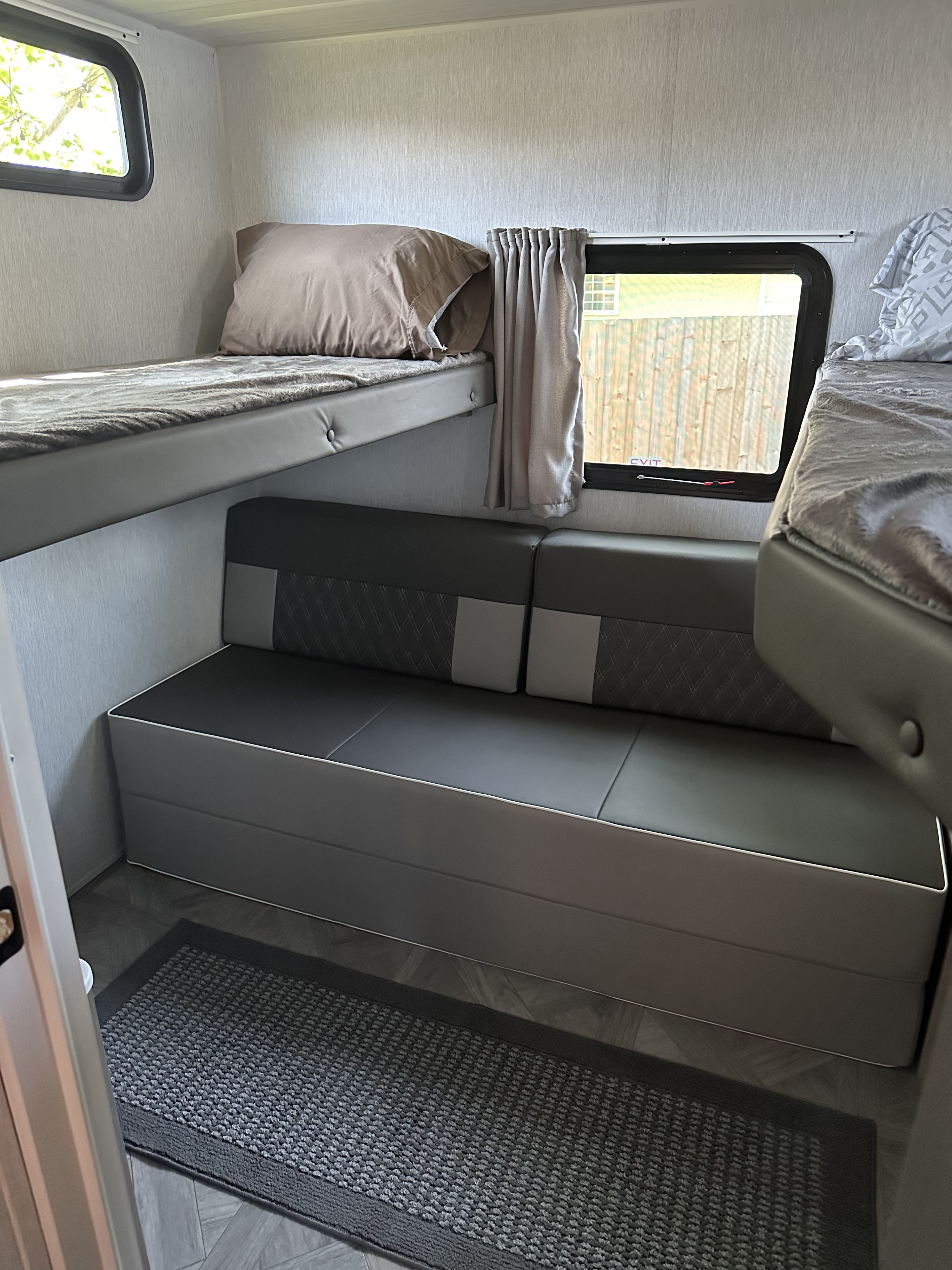 Modern RV rental interior: comfortable bunk beds, a gray sofa/dinette below, and a window with curtains.. Forest River Cruise Lite 2023