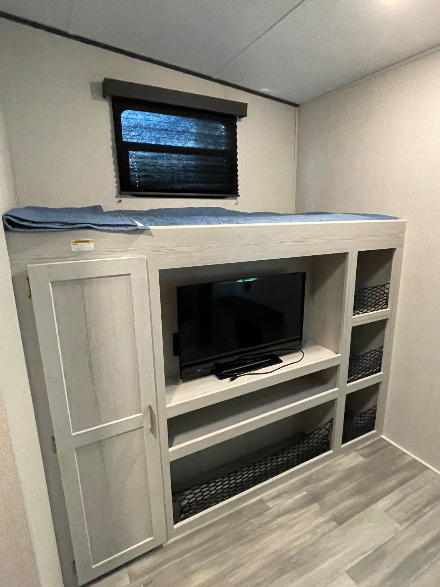 This RV rental's compact interior features a top bunk with a blue blanket, TV, cabinet, and netted storage cubbies.. Keystone RV Sprinter 2021