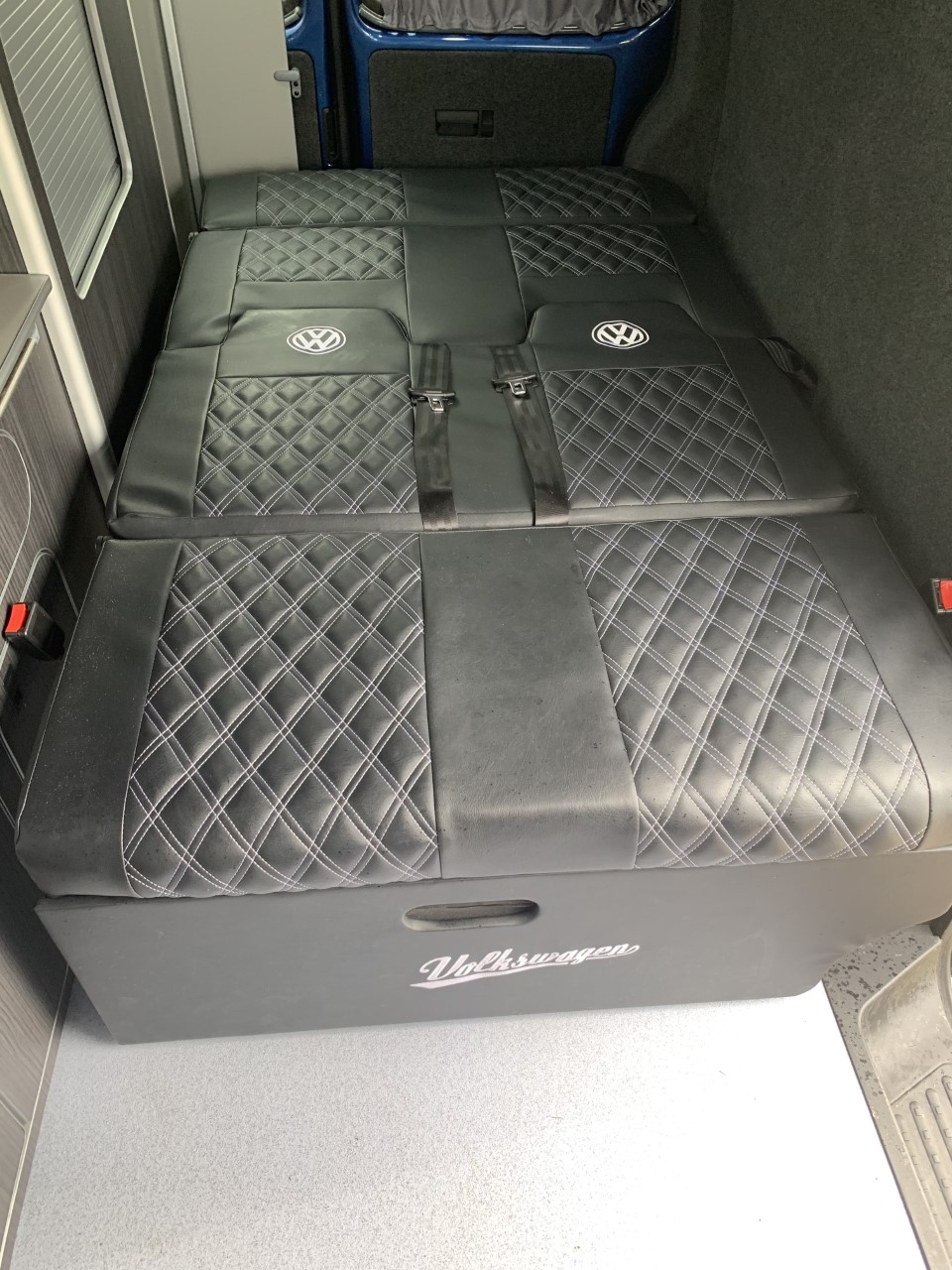 Stylish black quilted Volkswagen campervan bed/seating with seatbelts, perfect for an RV rental adventure.. Volkswagen T5 2014