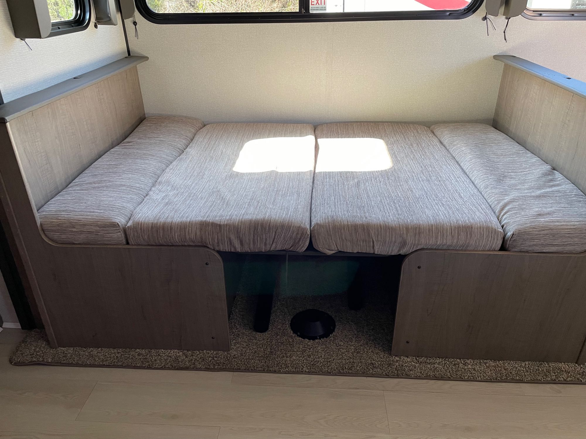 Cozy RV rental interior showing a dinette with light fabric cushions, convertible to a bed, bathed in sunlight. Wood trim and windows visible.. Keystone RV Hideout 2021