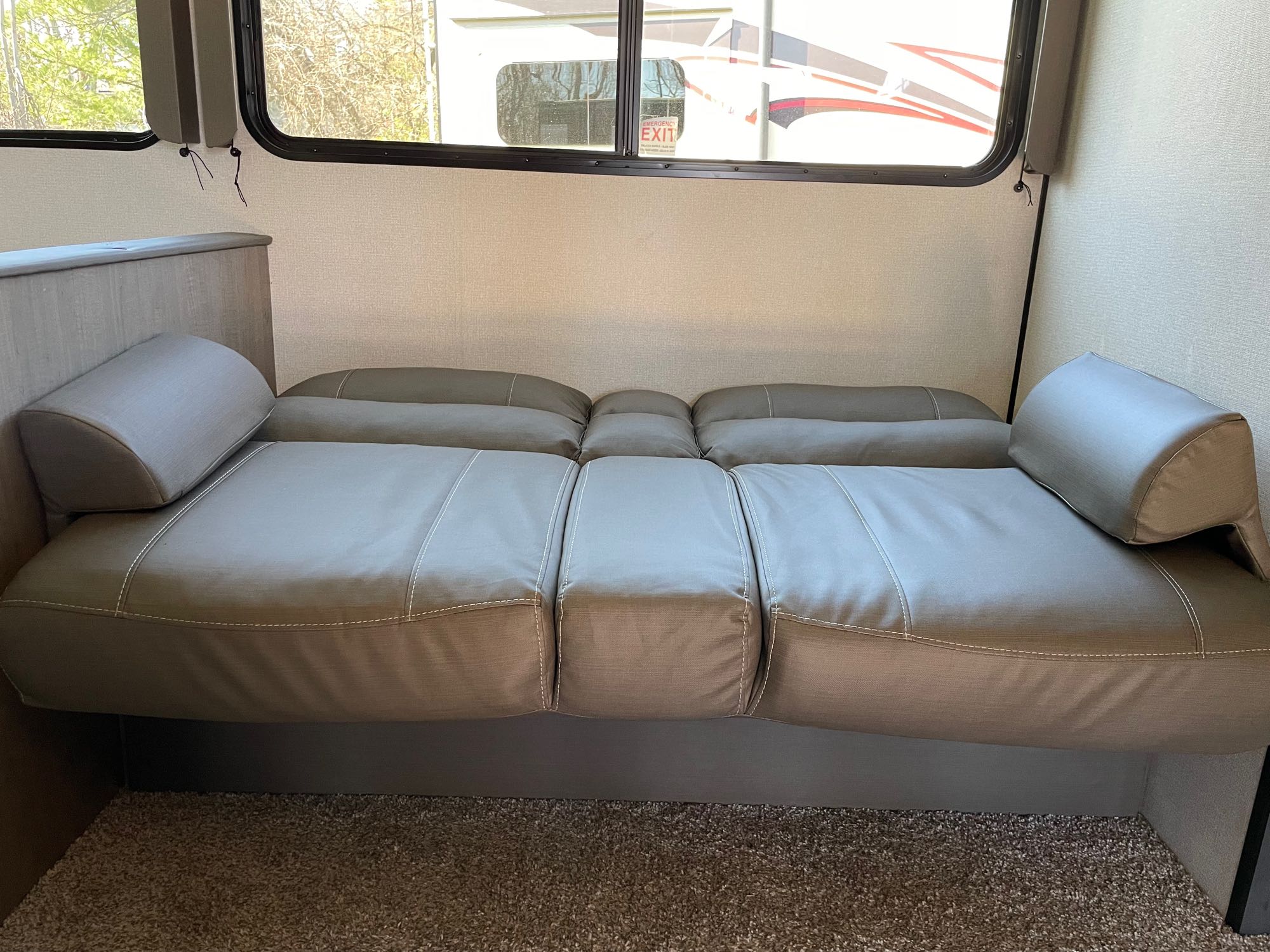 RV rental interior: A grey sofa/convertible bed with pillows, under a large window showing trees and another vehicle outside.. Keystone RV Hideout 2021