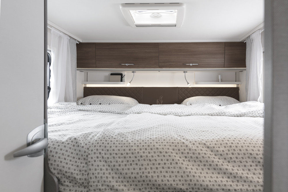 Inside an RV rental: A bright, modern bedroom with a large bed, brown headboard, and overhead storage.. Etrusco Etrusco T7400SBC 2021