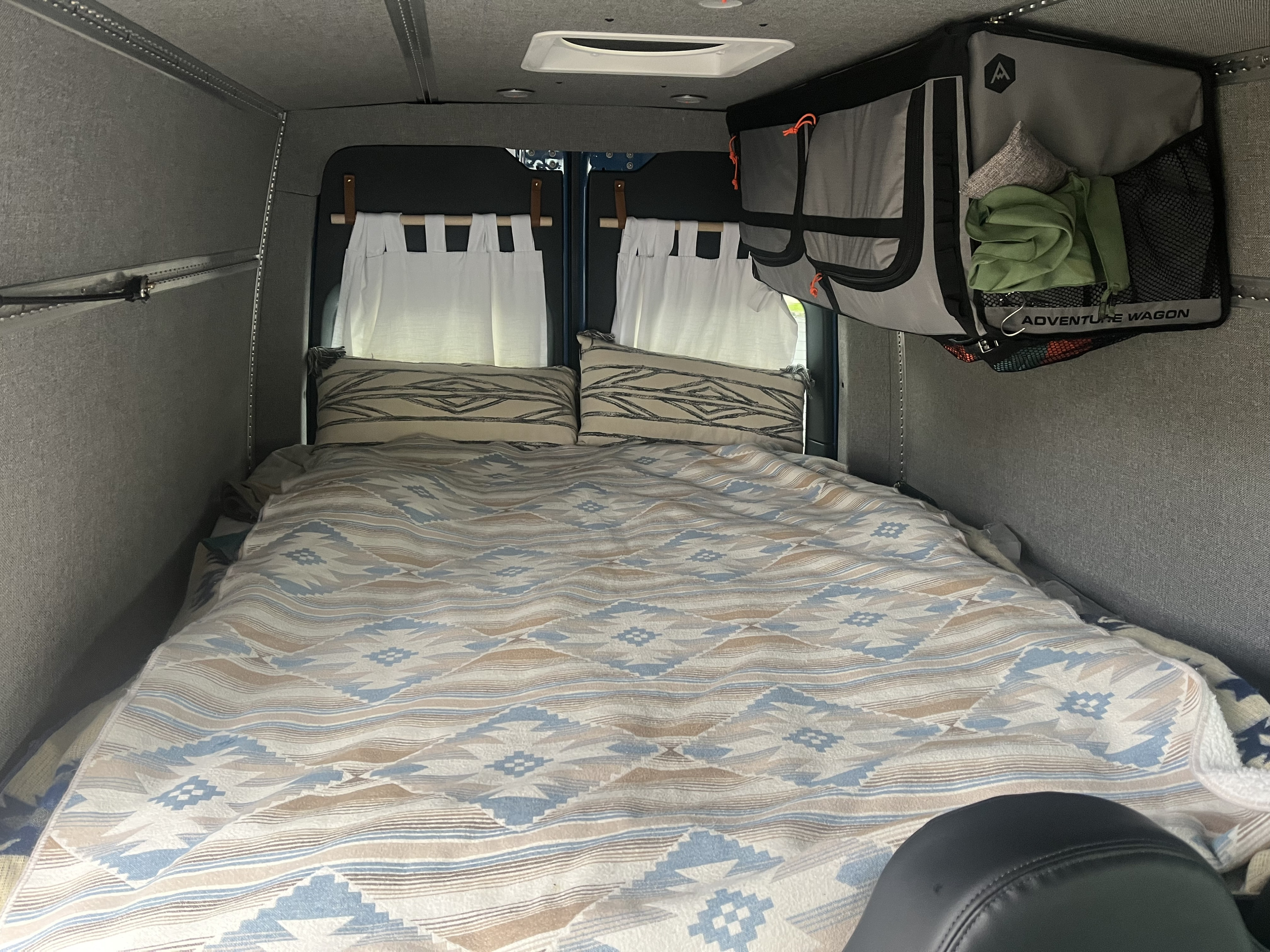 Cozy RV rental sleeping area features patterned bedding, pillows, and hanging storage.. Mercedes-Benz Sprinter 2021