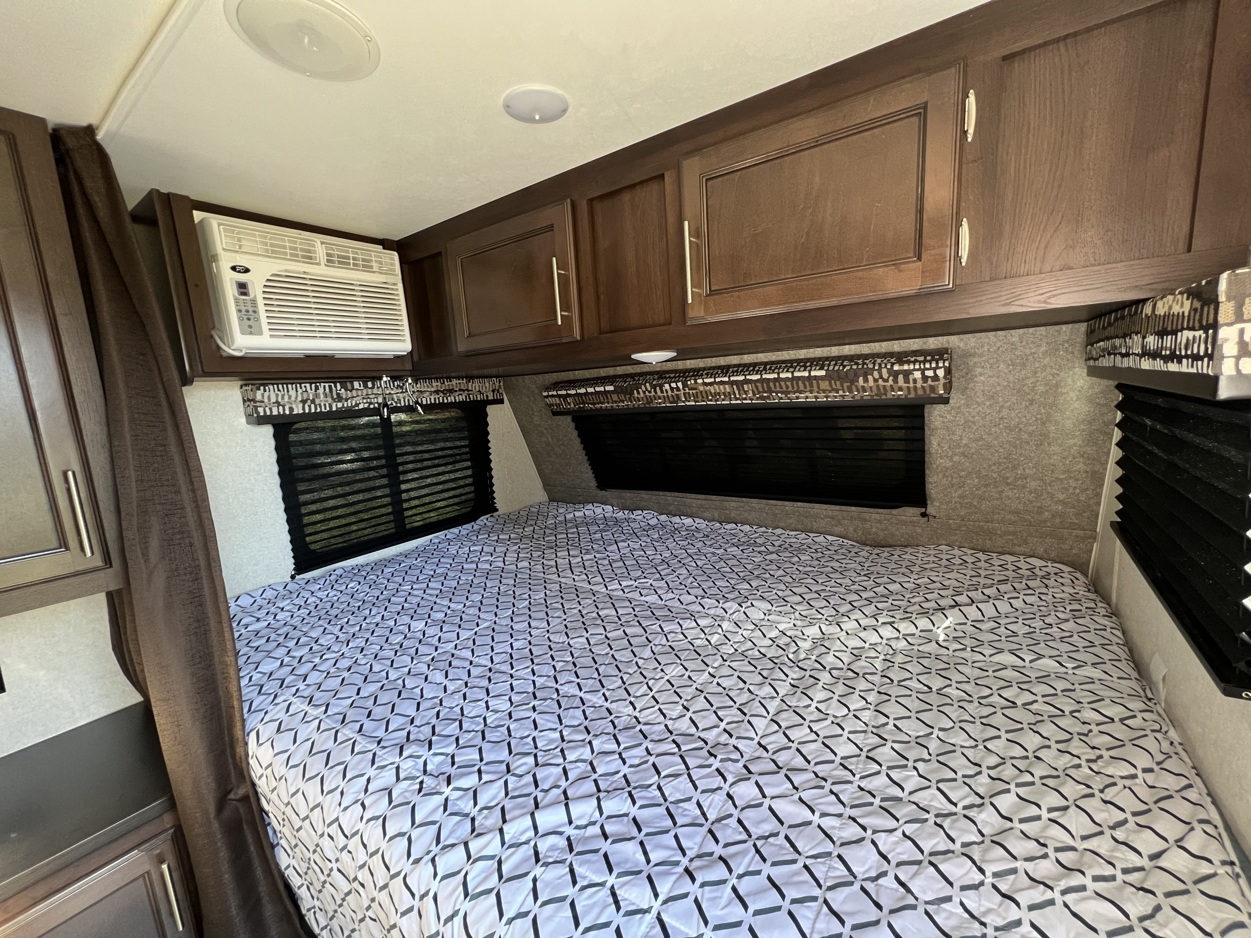 Cozy RV bedroom with patterned bed, overhead wood cabinets, integrated AC, and windows, great for an rv rental.. Jayco Jay Flight SLX 2019