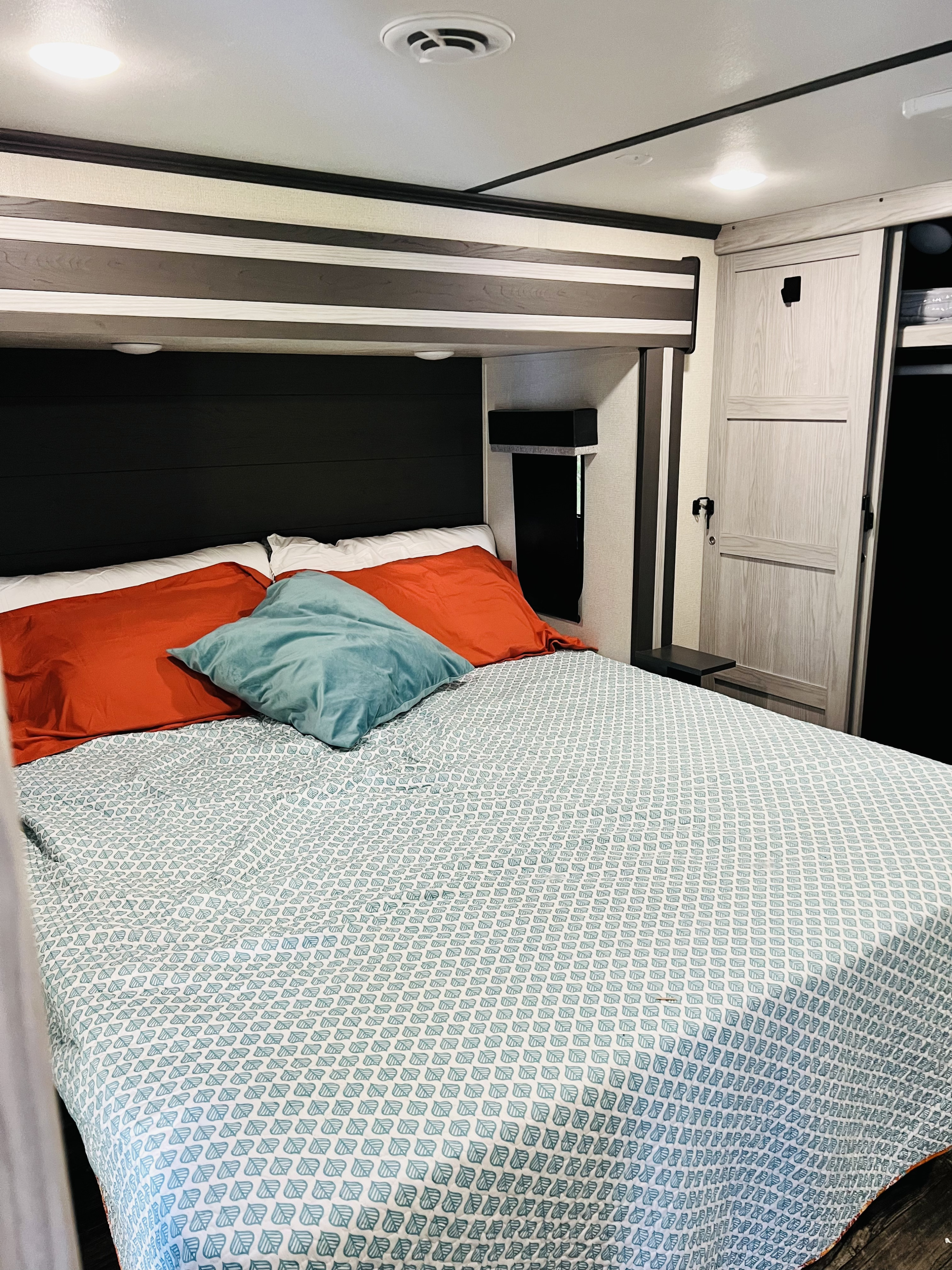 Cozy bedroom in an RV rental, featuring a comfortable bed with colorful bedding and practical overhead storage.. Keystone Fuzion 2022