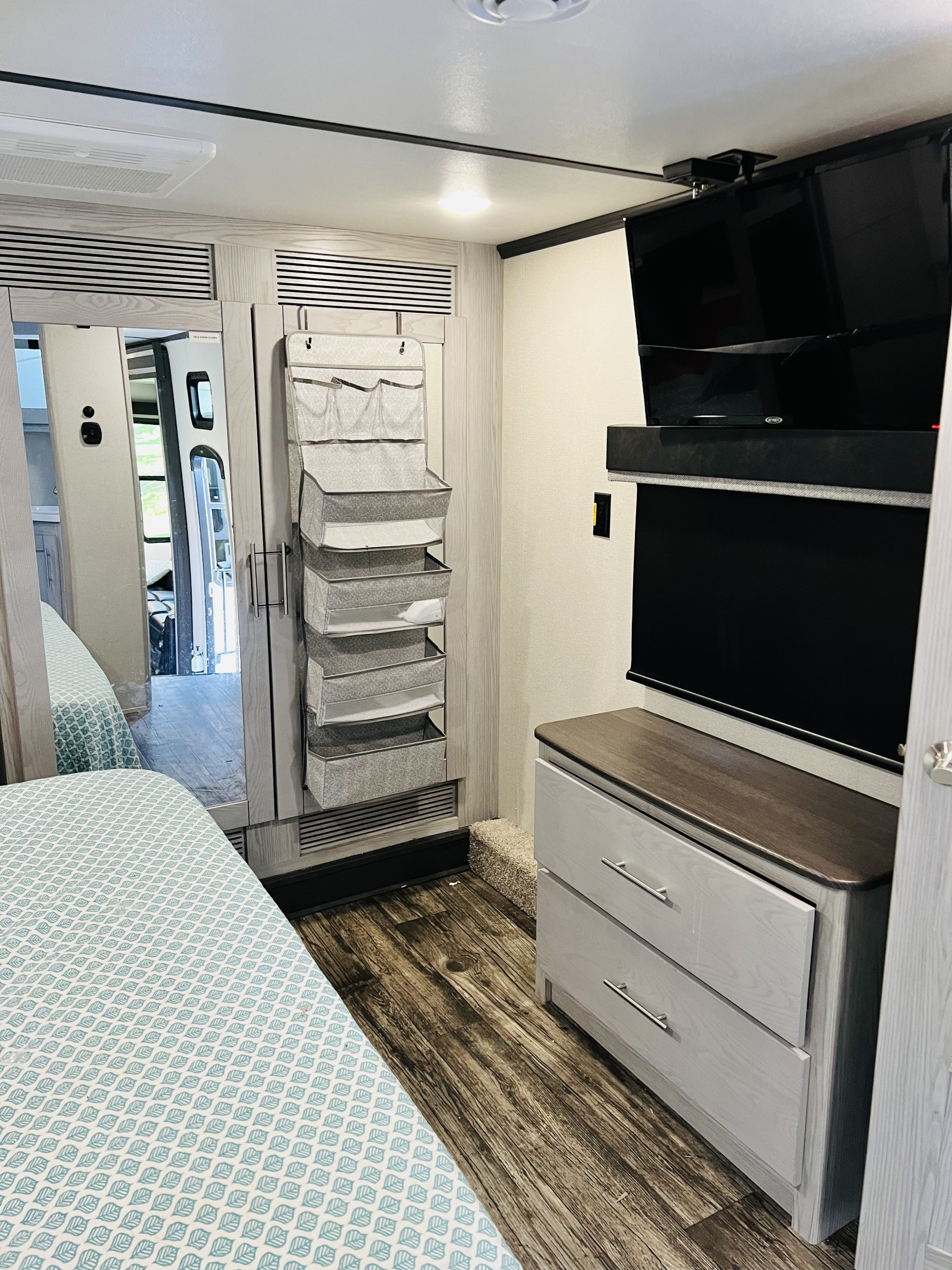 Step into this modern RV rental bedroom featuring a bed, ample storage, TV, dresser, and full-length mirror.. Keystone Fuzion 2022