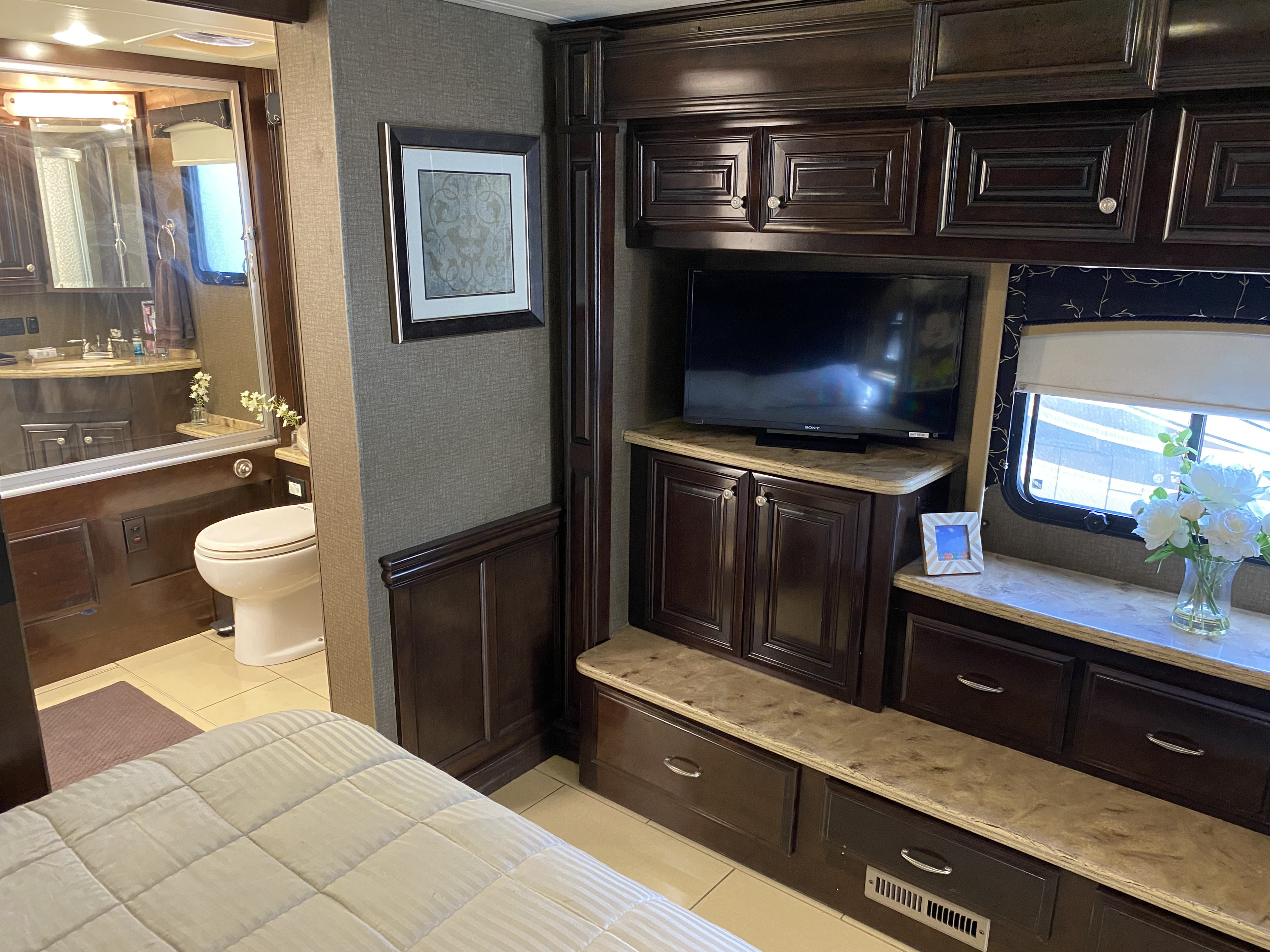 RV rental bedroom featuring a flat-screen TV, rich wood cabinets, and a glimpse of the private bathroom.. Thor Motor Coach Tuscany 2015