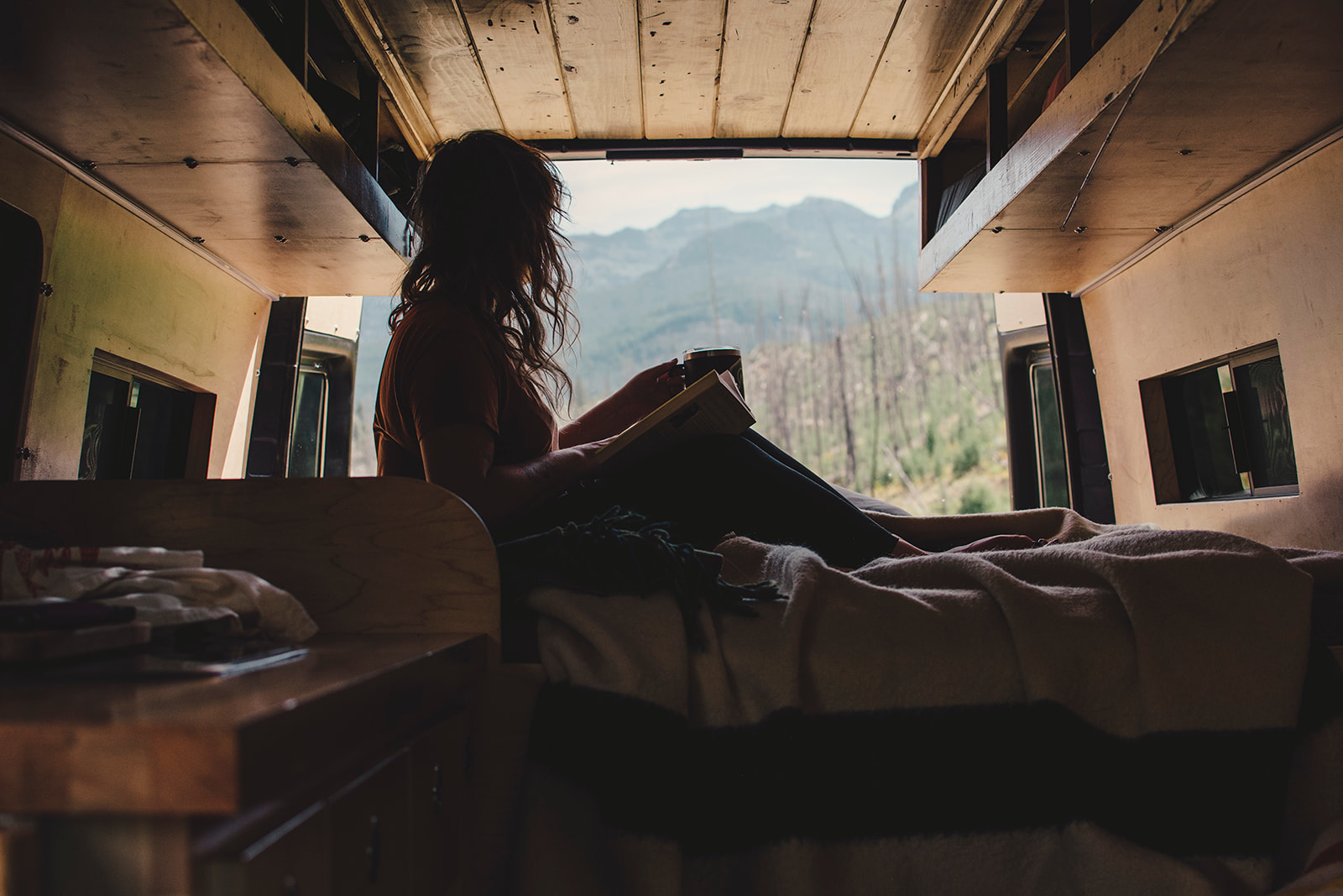 Relaxing in an rv rental, a person reads a book enjoying mountain views. Perfect van life adventure.. Mercedes-Benz Sprinter 2006