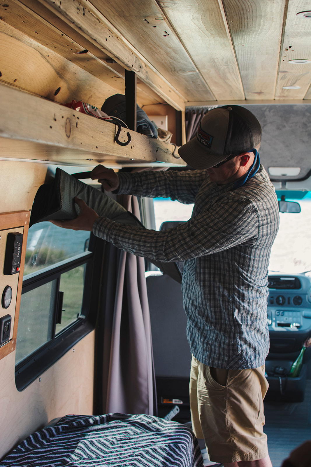 A man organizes overhead storage in a cozy RV rental, showing practical van interior design & wood accents.. Mercedes-Benz Sprinter 2006