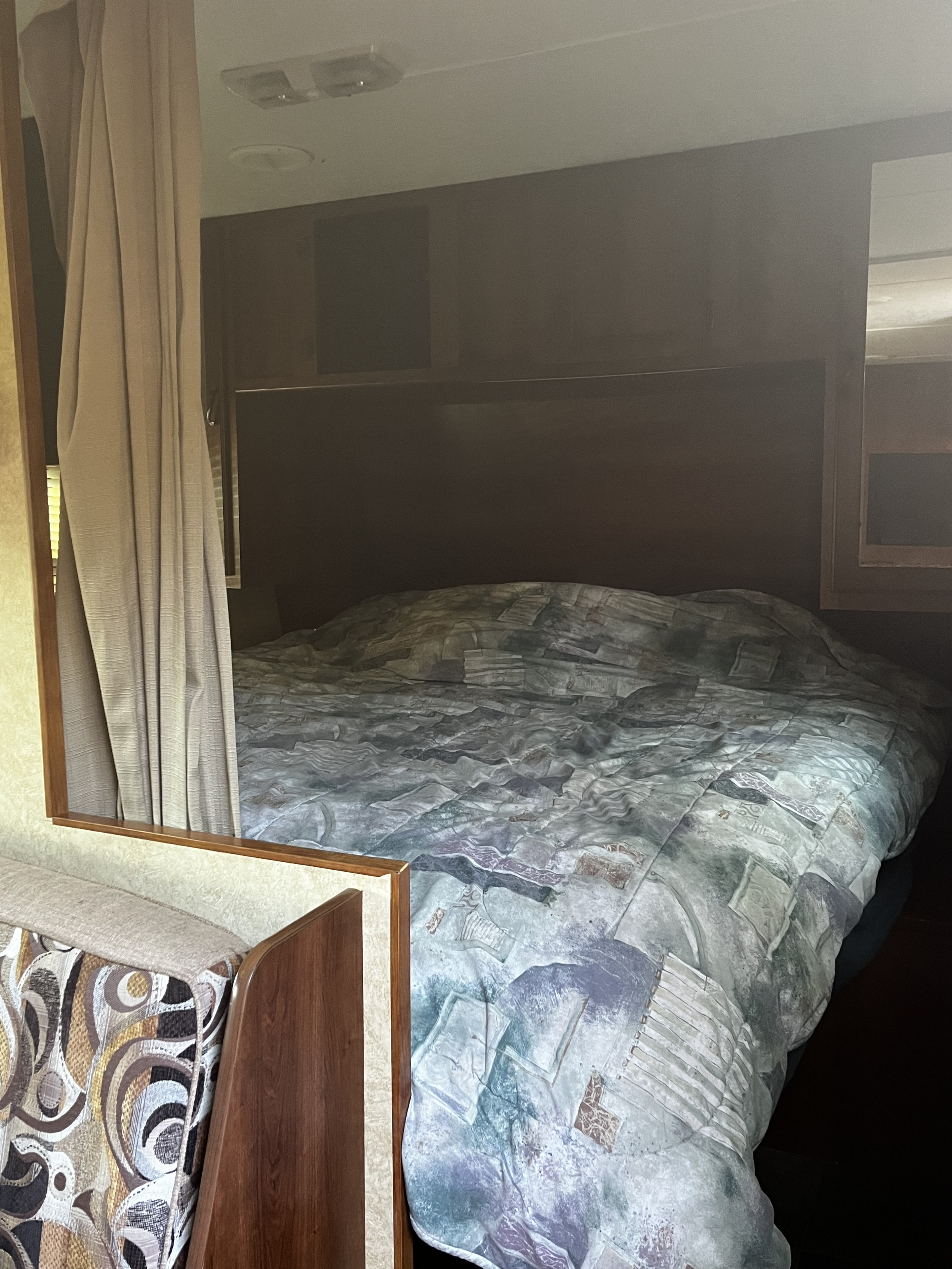 RV rental's bedroom: a large bed with an abstract quilt, dark wood headboard, and a privacy curtain.. Avenger LT 2012
