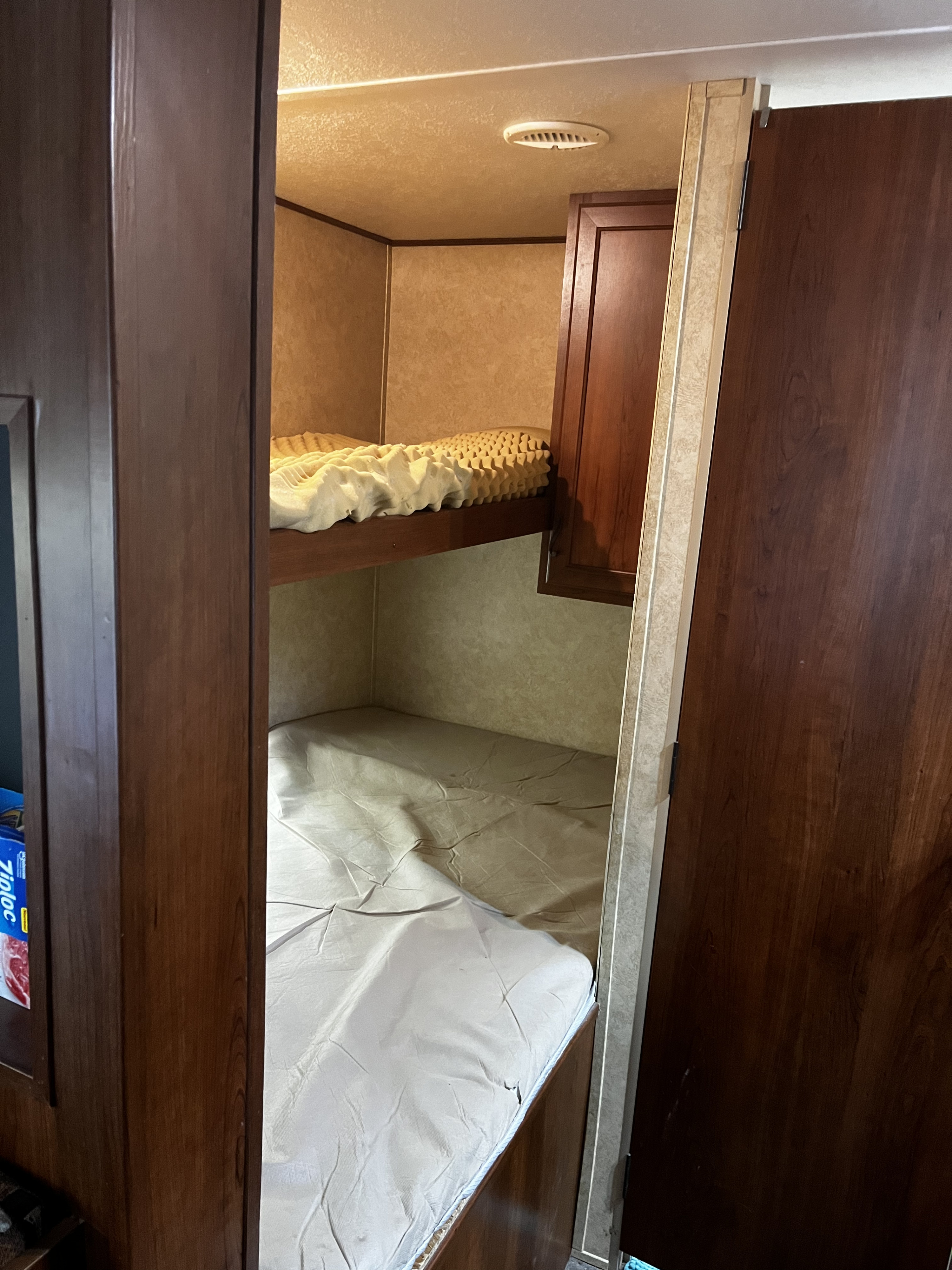 Inside an RV rental, showcasing cozy upper and lower bunk beds with mattresses and built-in cabinetry for travel accommodation.. Avenger LT 2012