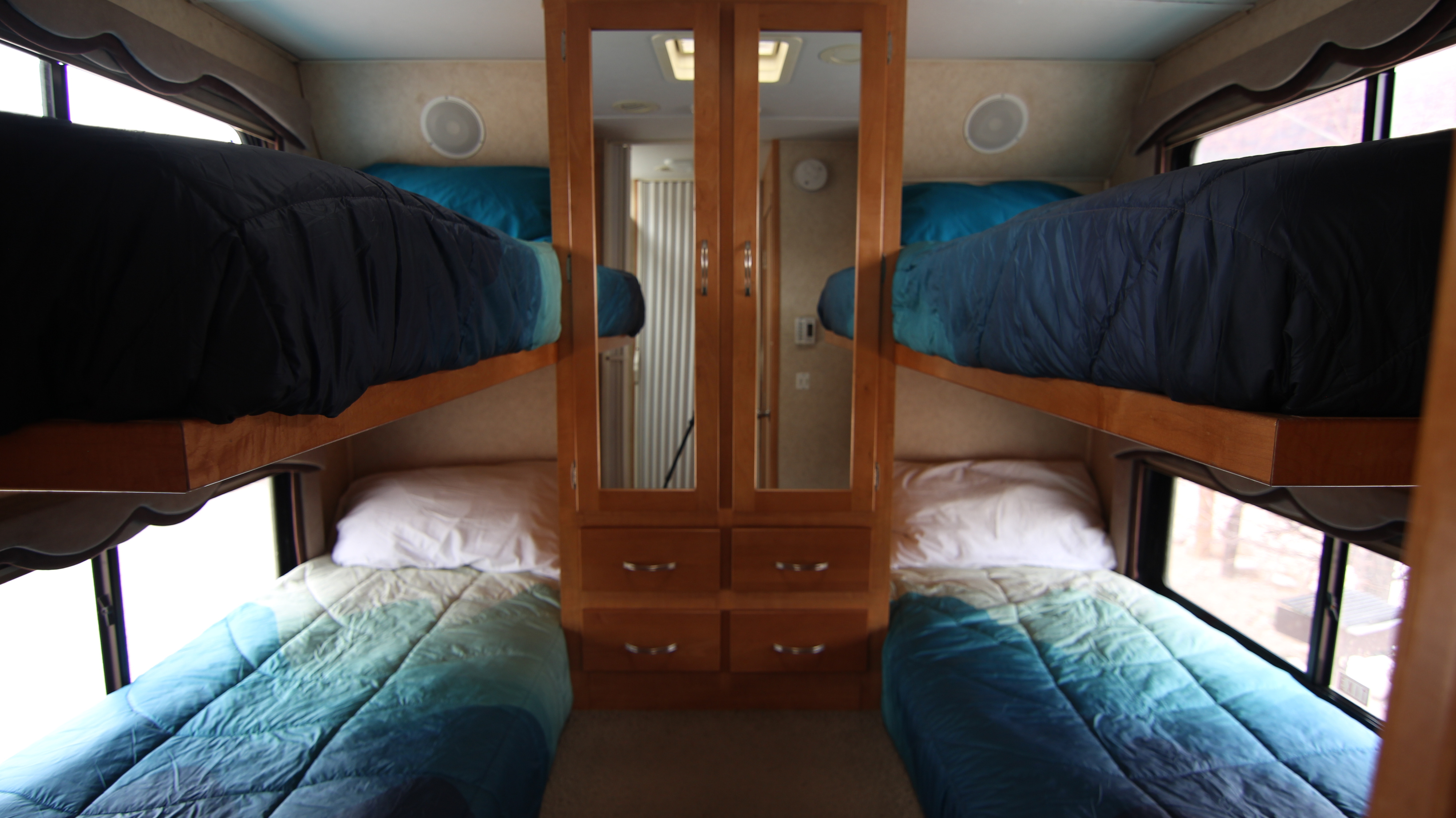 RV rental bunk beds: Four sleeping berths (2 up, 2 down) with blue bedding, flanking a central mirrored cabinet.. Forest River Sunseeker 2008