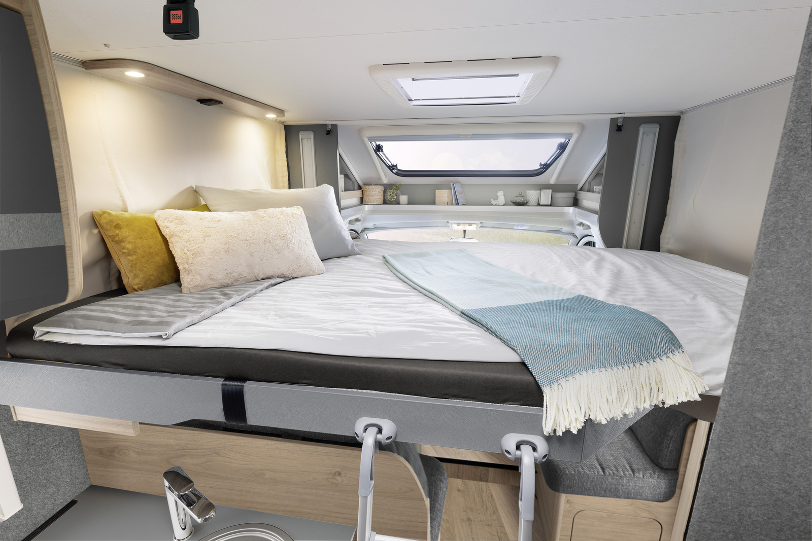 Cozy RV rental bedroom inside a camper, featuring a comfortable bed, panoramic window, skylight, and integrated kitchen area.. Dethleffs Just Go T 7055 EB 2023