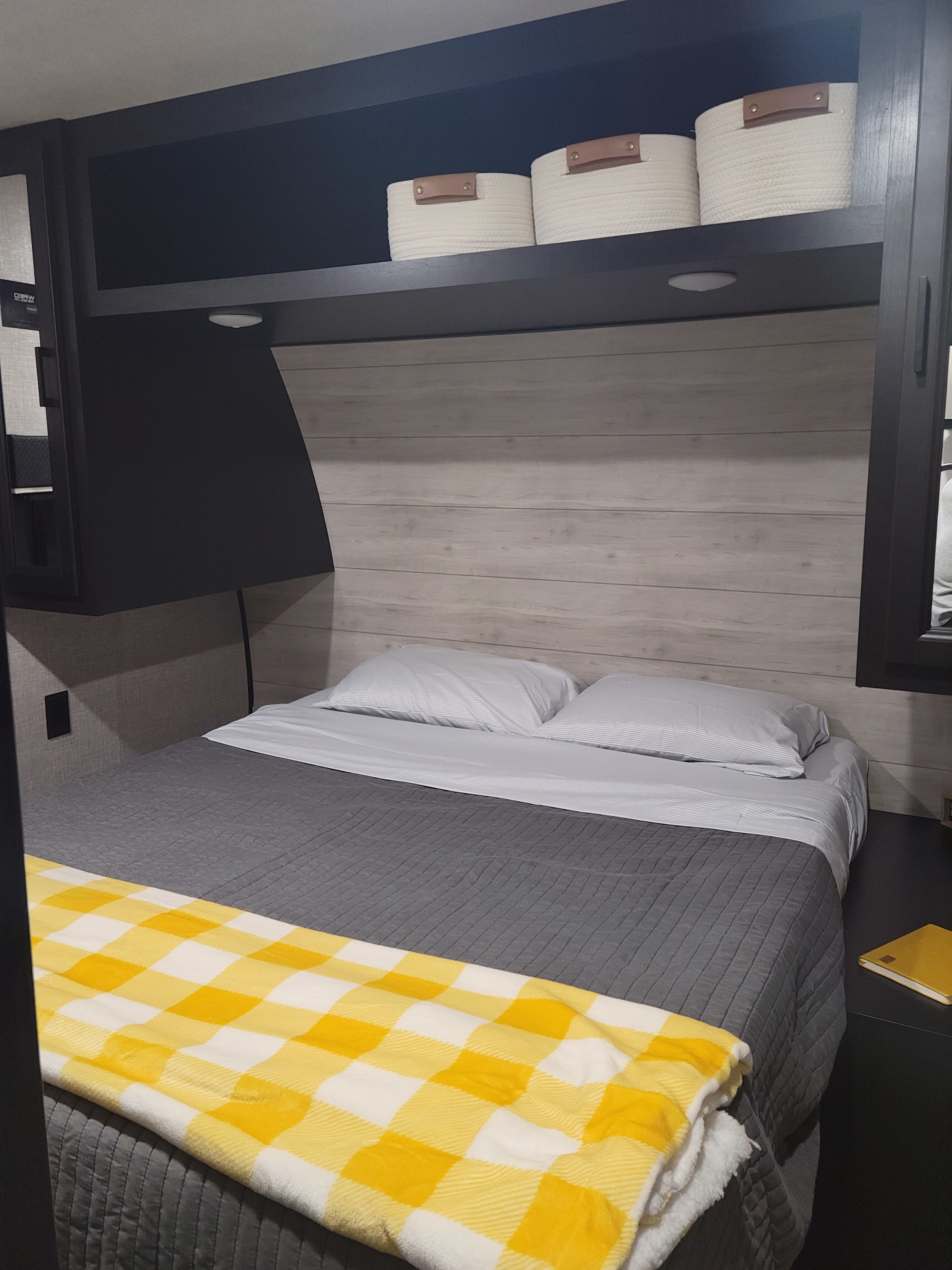 Experience comfort in our RV rental! This cozy RV bed offers soft grey bedding, a cheerful yellow throw, and overhead storage.. Jayco Jay Flight 2023