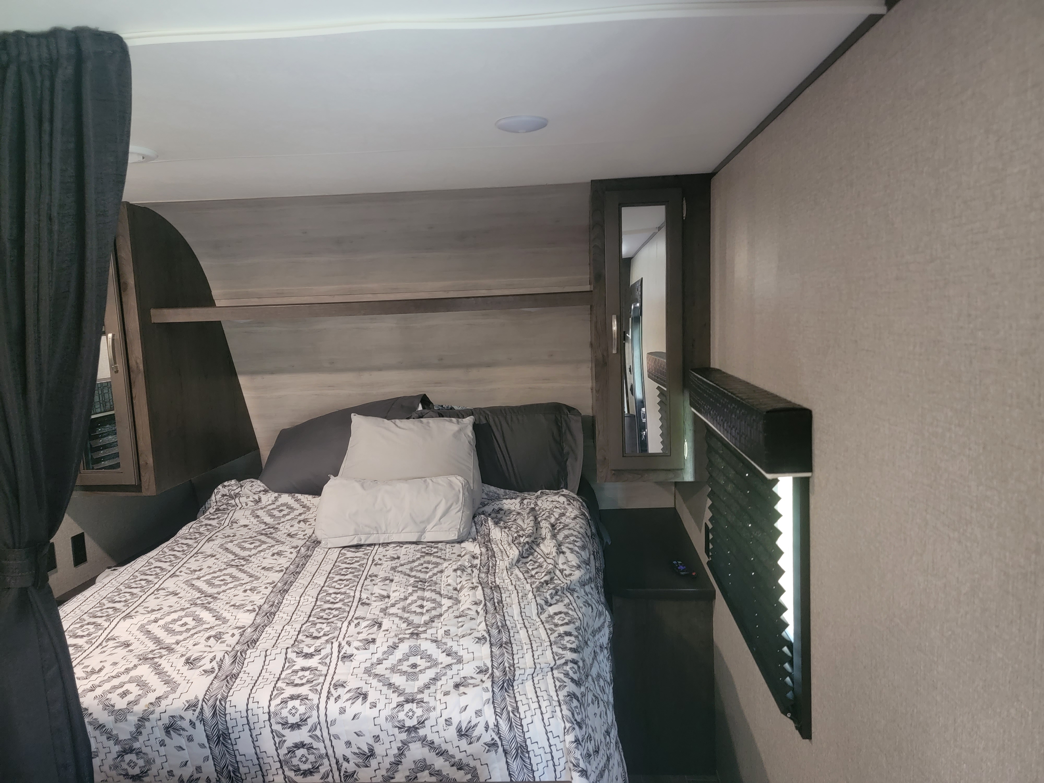 Comfortable RV rental bedroom with patterned bedding, built-in storage, and a mirror, ideal for travel.. Jayco Jay Flight 2021