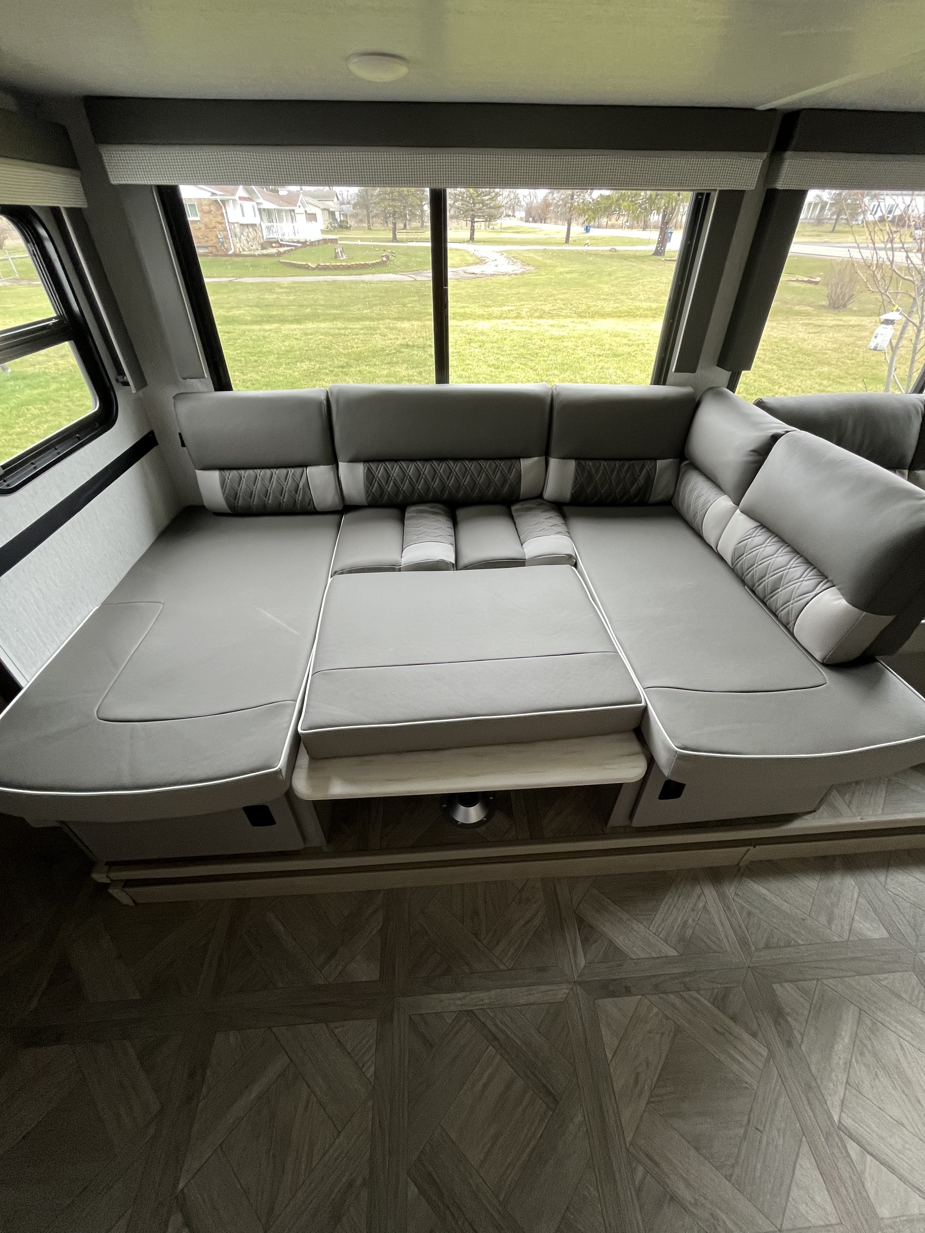 Comfortable RV rental living space: a large gray convertible sofa/bed by windows overlooking a green lawn.. Wildwood X-Lite BH 263 2023