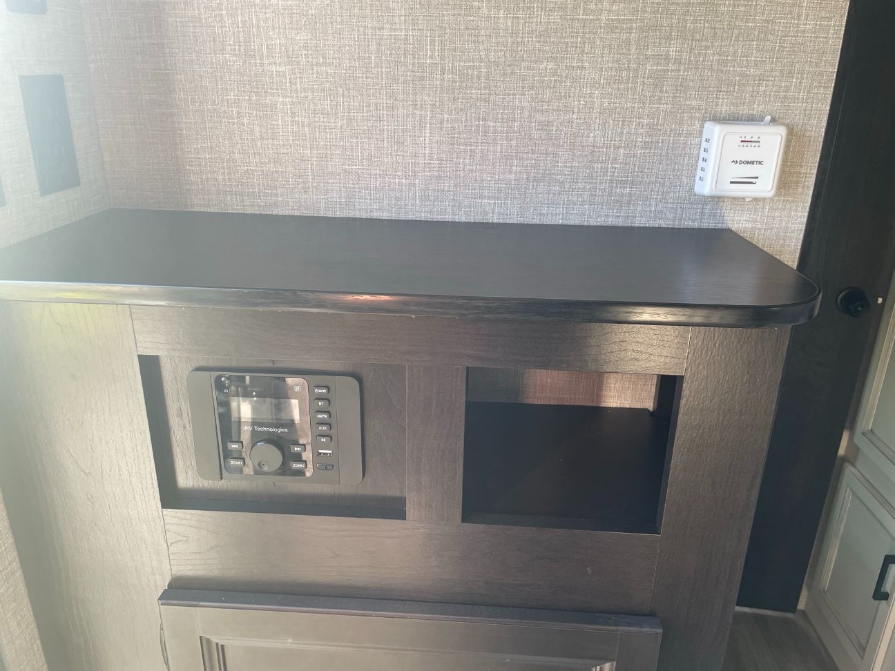 RV rental interior showing an iRV Technologies stereo, a Dometic thermostat, and storage cubby on a dark cabinet.. Jayco Jay Flight SLX 2022