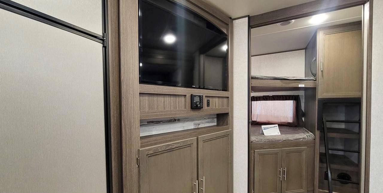 RV rental interior featuring a wooden entertainment center with TV and storage, next to bunk beds with a ladder. Perfect for trips.. Dutchmen Kodiak Ultra Lite 2020