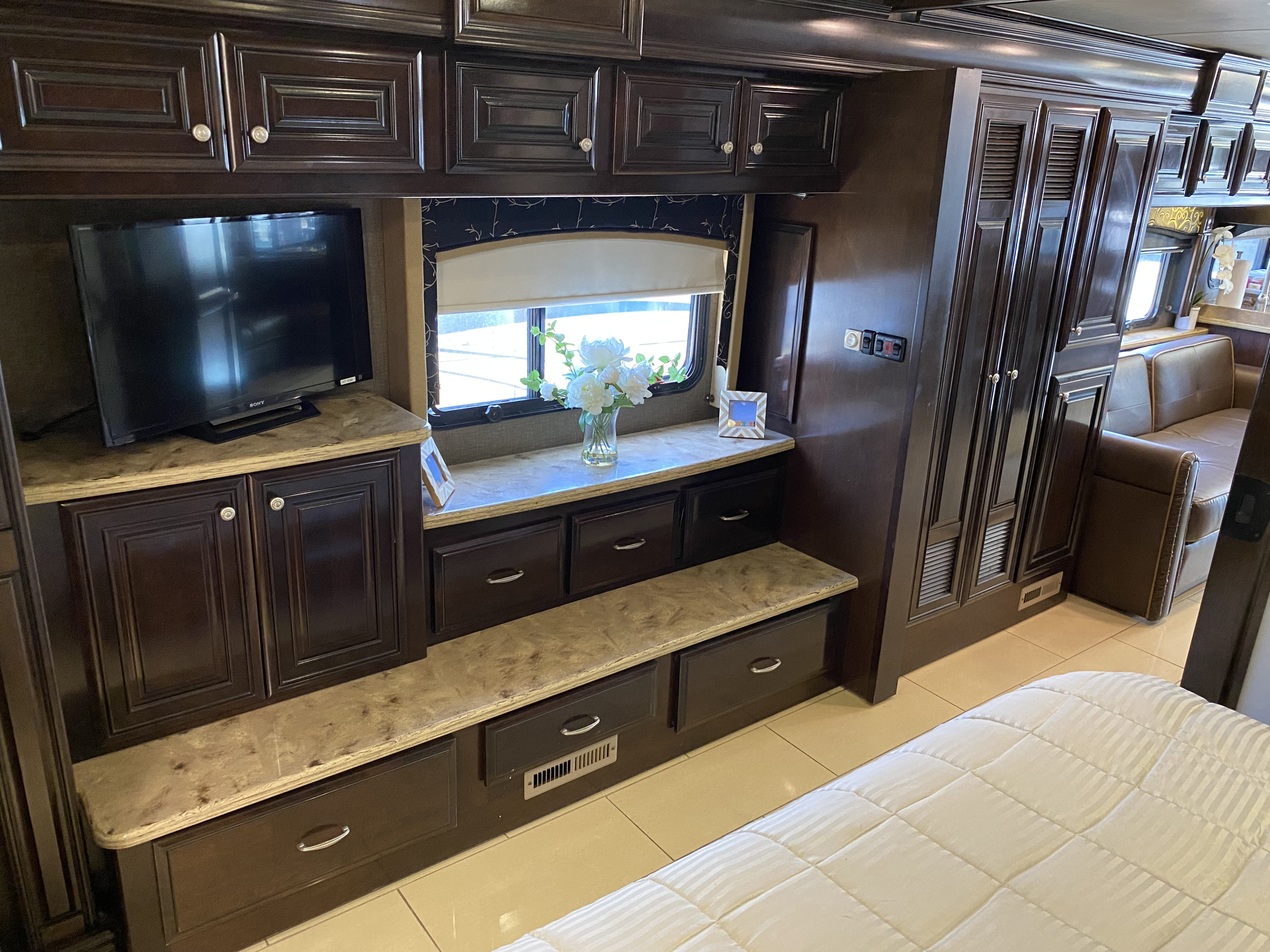 Luxurious RV rental bedroom area featuring dark wood cabinets, a TV, scenic window, and a comfortable bed.. Thor Motor Coach Tuscany 2015