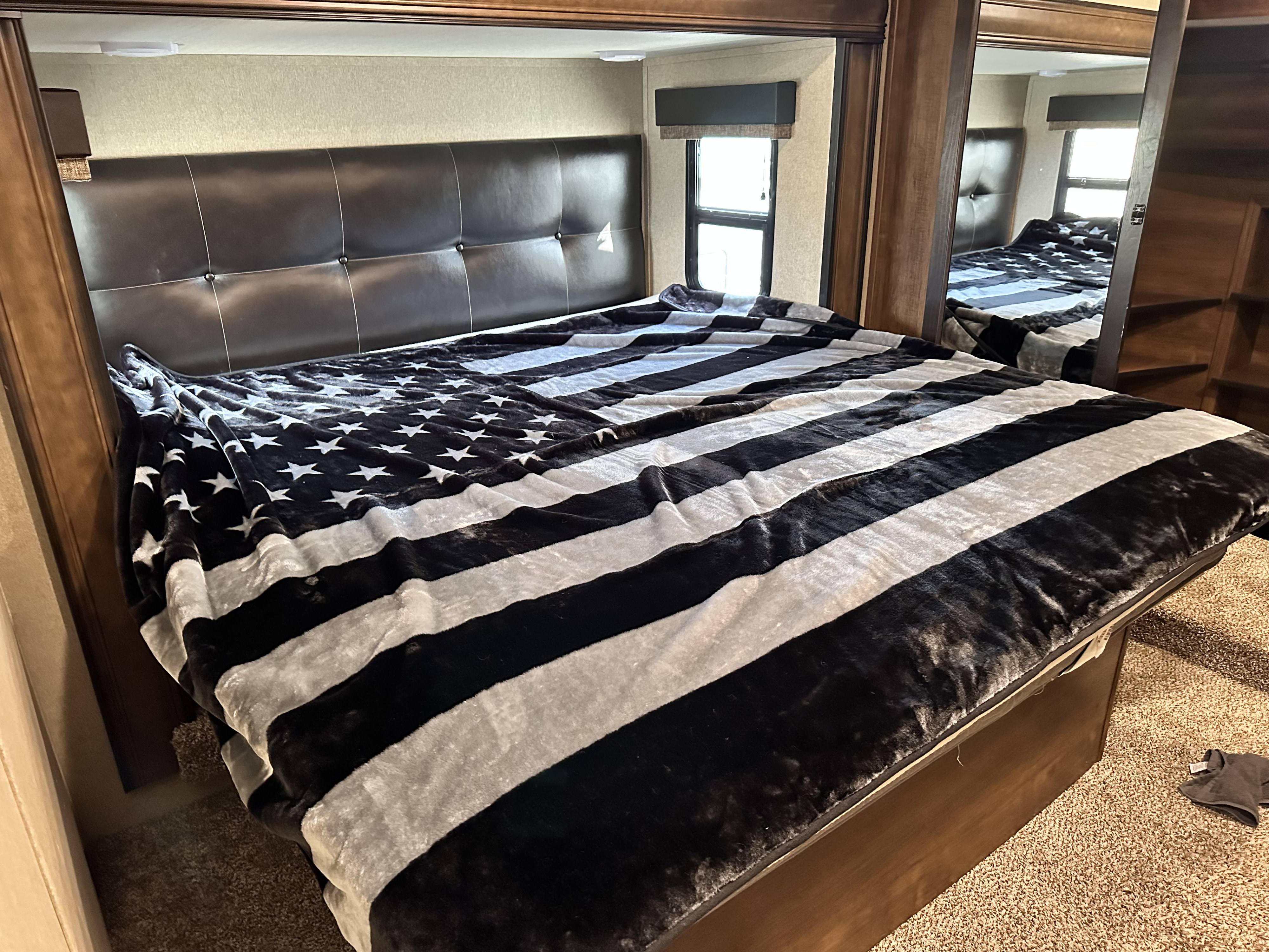 Cozy RV rental bedroom featuring a large bed with a black & white flag blanket & dark headboard.. Grand Design Reflection 2020