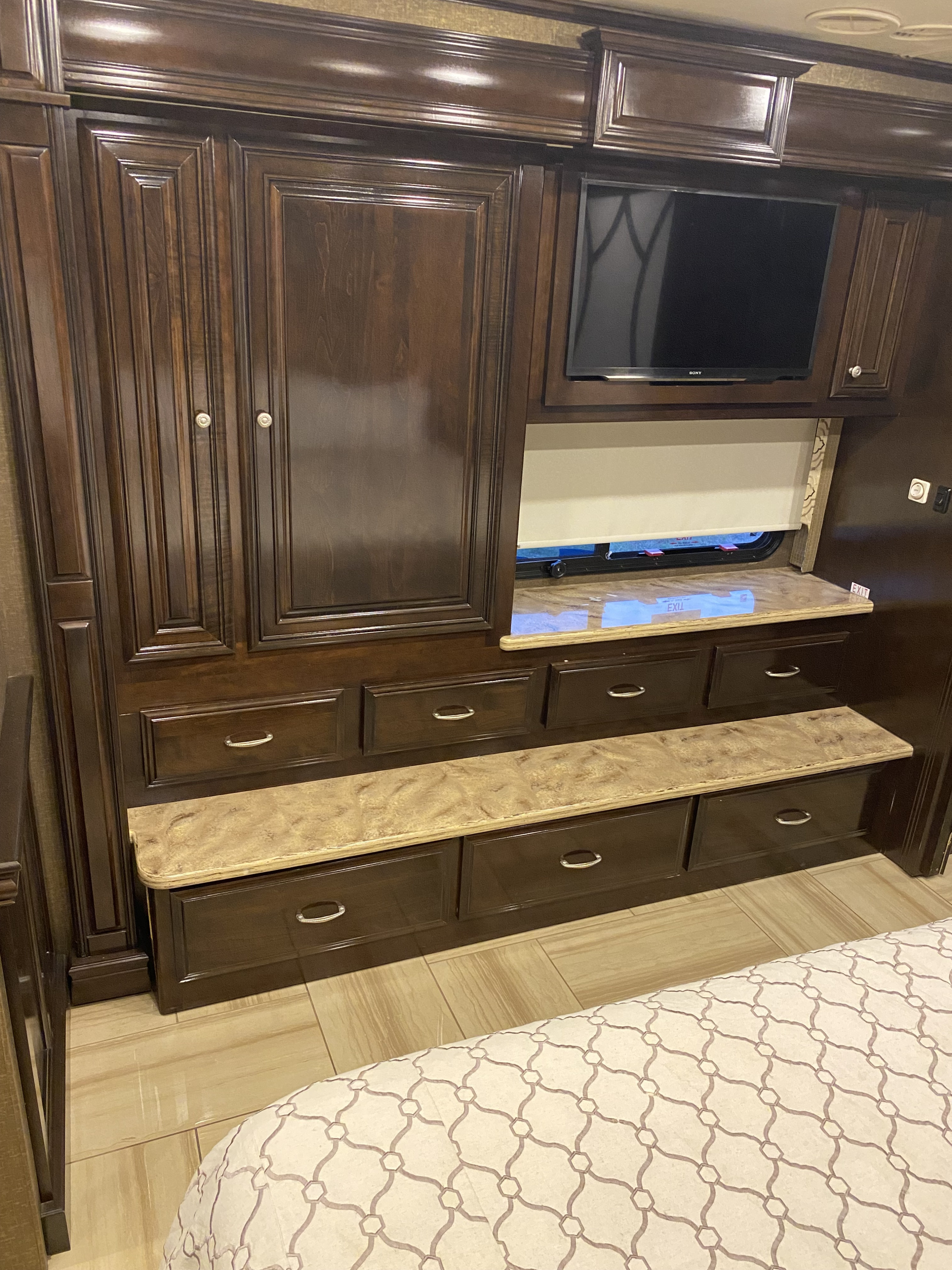 Dark wood cabinetry with built-in storage and a TV in an RV rental bedroom, showcasing a window, bed, and tiled floor.. Thor Motor Coach Tuscany 2016