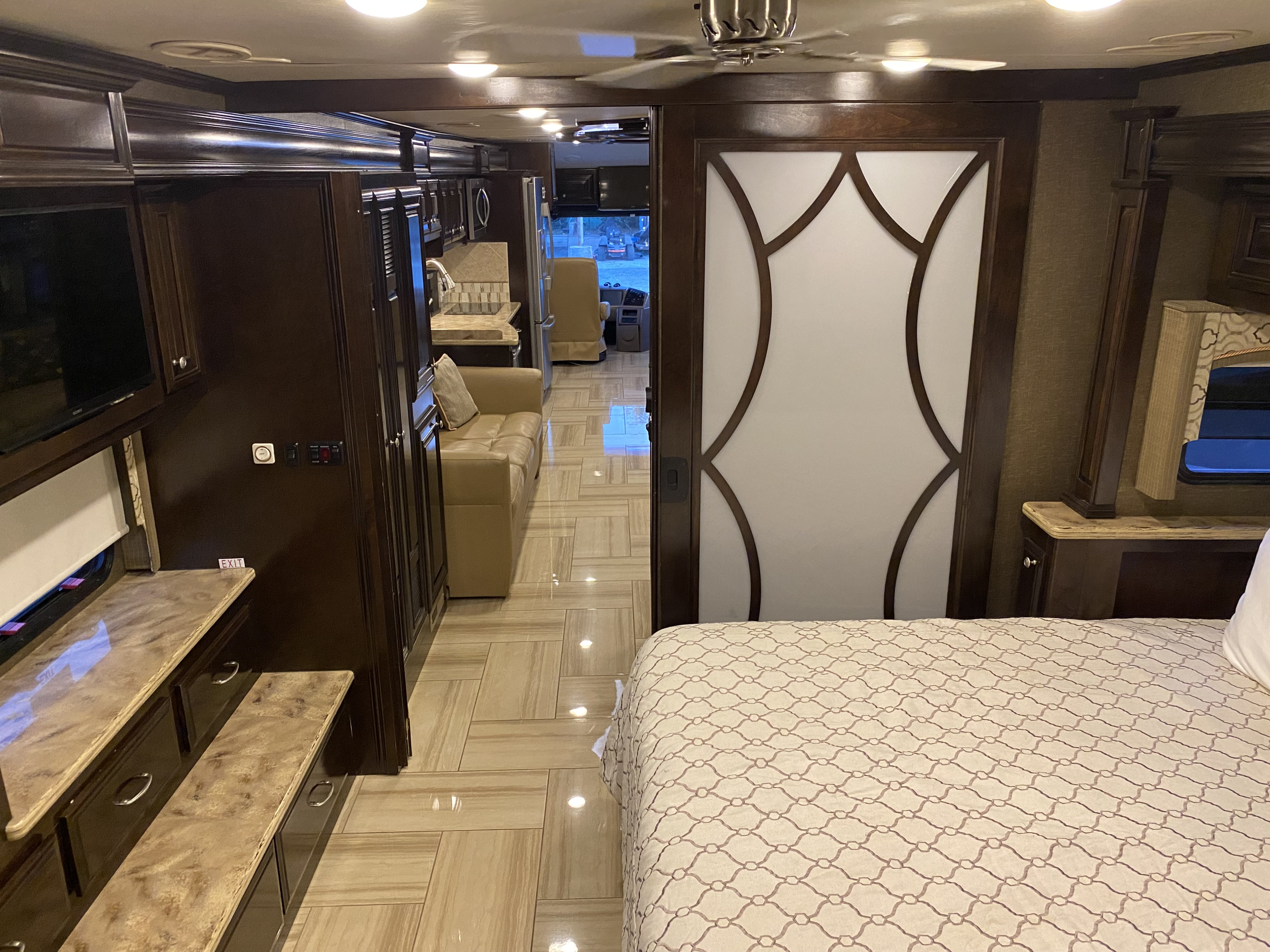 Spacious, luxurious RV rental interior featuring a bedroom, kitchen, and living area, with elegant wood cabinetry and tile flooring.. Thor Motor Coach Tuscany 2016