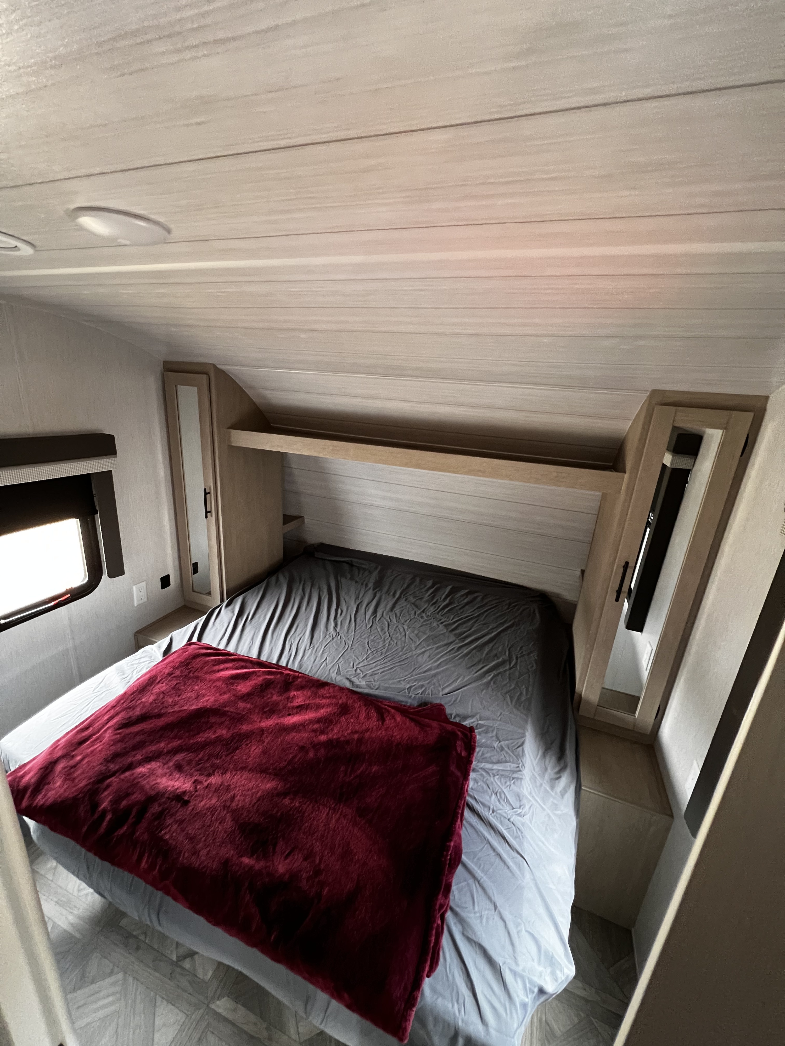 Cozy RV rental bedroom with a bed, red blanket, overhead shelving, and a window, ideal for comfortable travel.. Forest River Salem Cruise Lite 2023