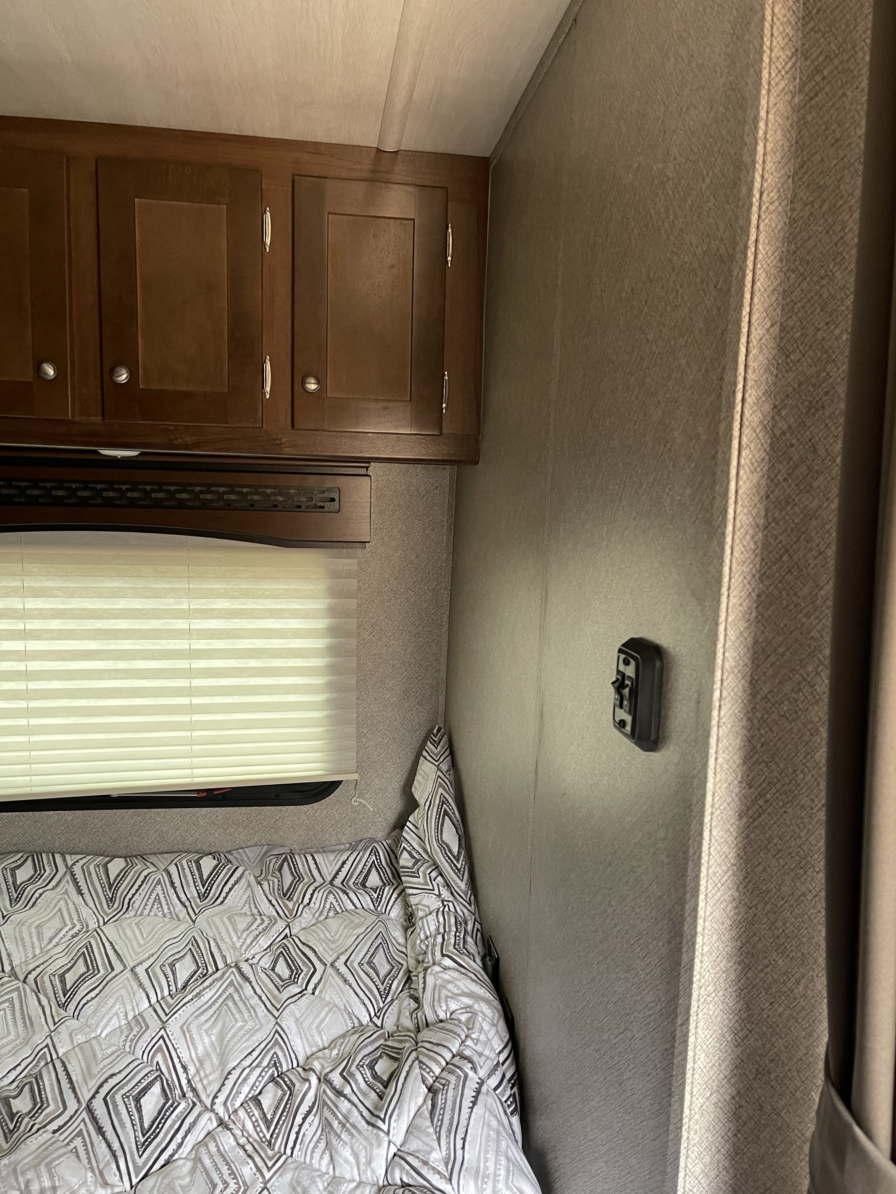 Inside an RV rental: cozy bedroom with a patterned bed, window blinds, overhead cabinets, and a wall switch.. Terry Other 2018