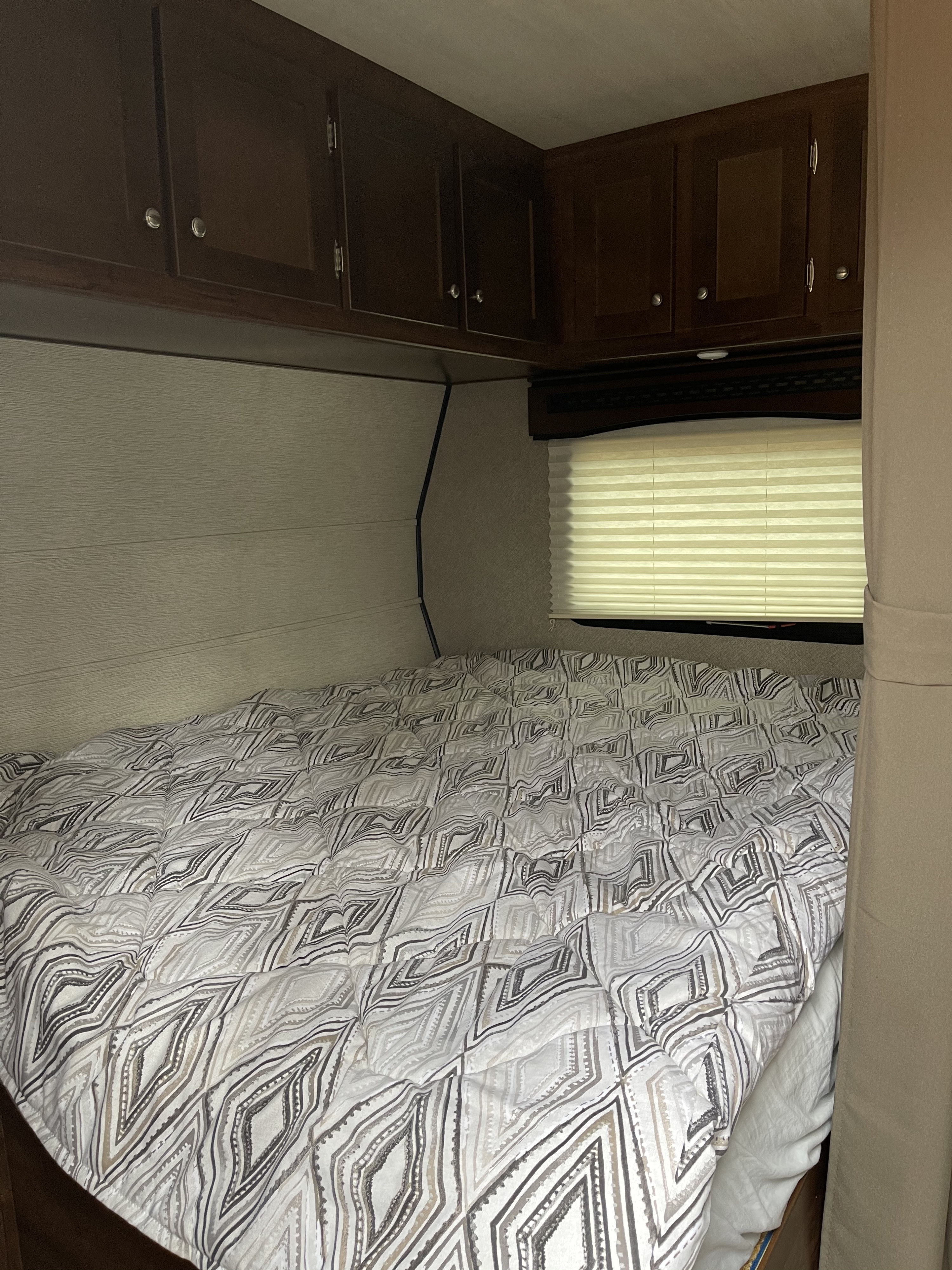 RV rental bedroom: Cozy sleeping area with patterned bedding, dark overhead cabinets, and a window blind.. Terry Other 2018