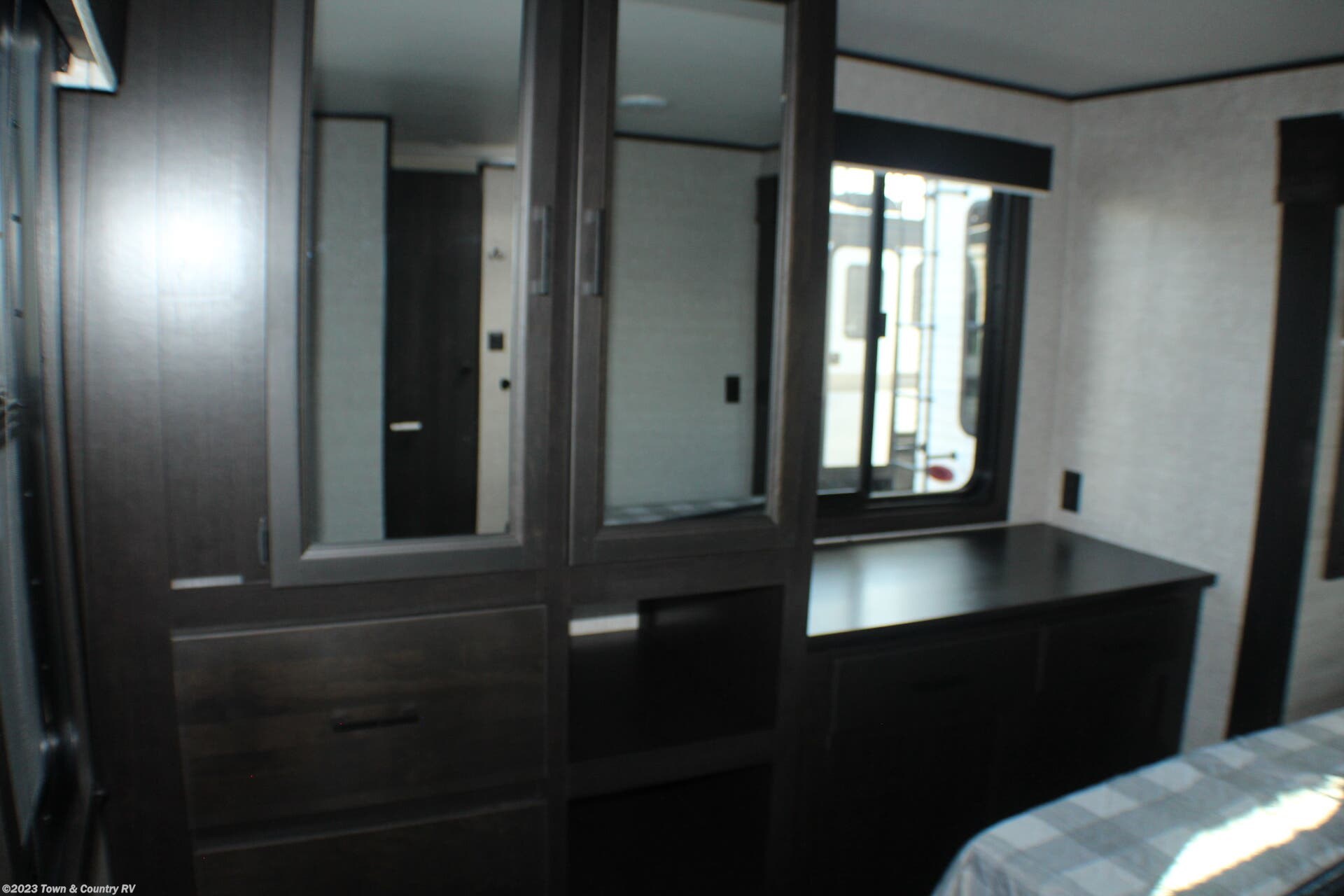 RV rental bedroom with dark wood built-in dresser, mirrors, window, and a glimpse of the bed.. Jayco Jay Flight 2022