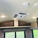 RV rental interior featuring a central AC unit, bright LED lights, and netted overhead storage above a window.. Forest River Rockwood Geo Pro 2018