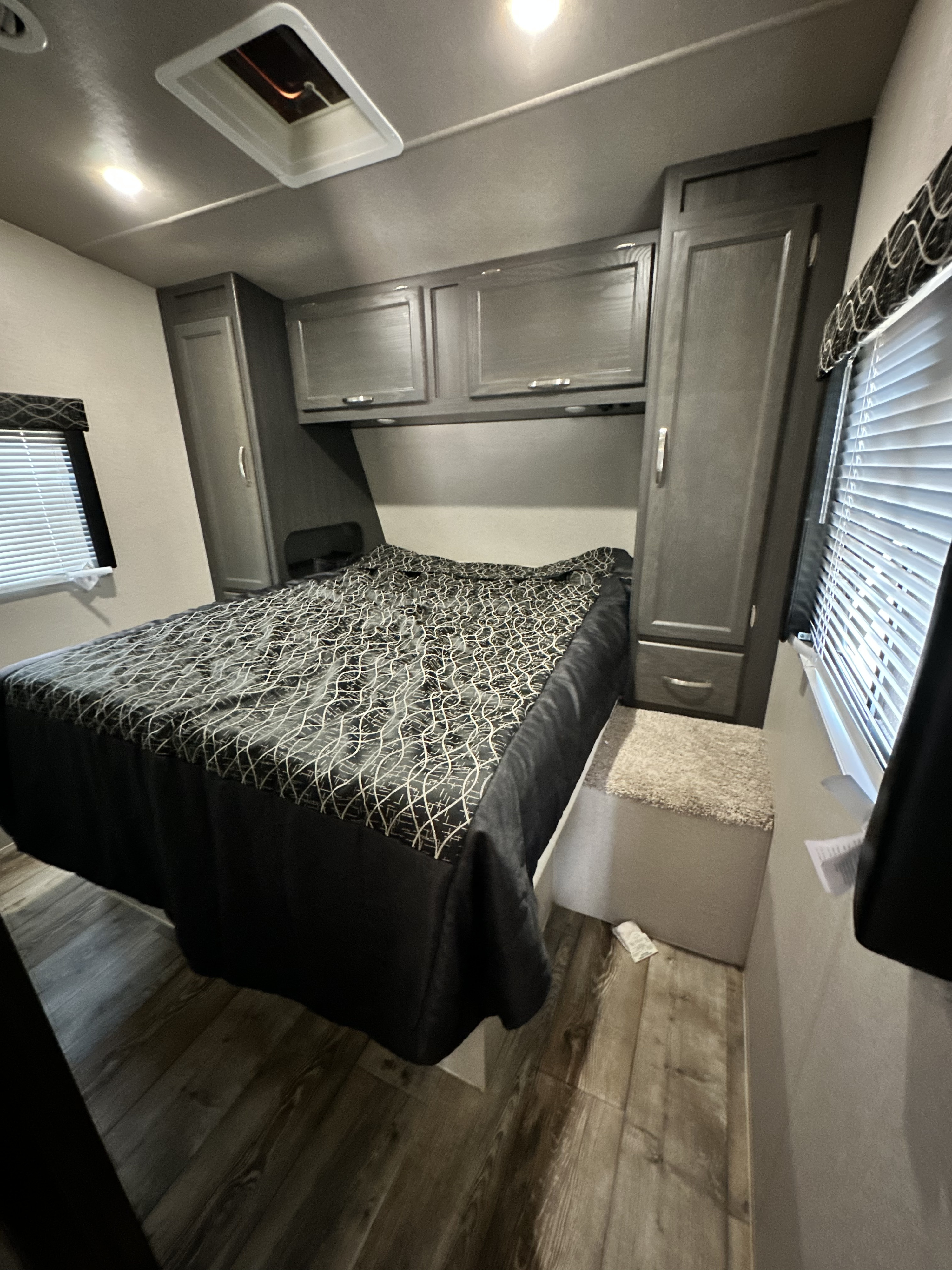 Cozy RV rental bedroom featuring a patterned bed, grey storage cabinets, and a window with blinds, all on wood-look flooring.. genesis supreme genesis 2017