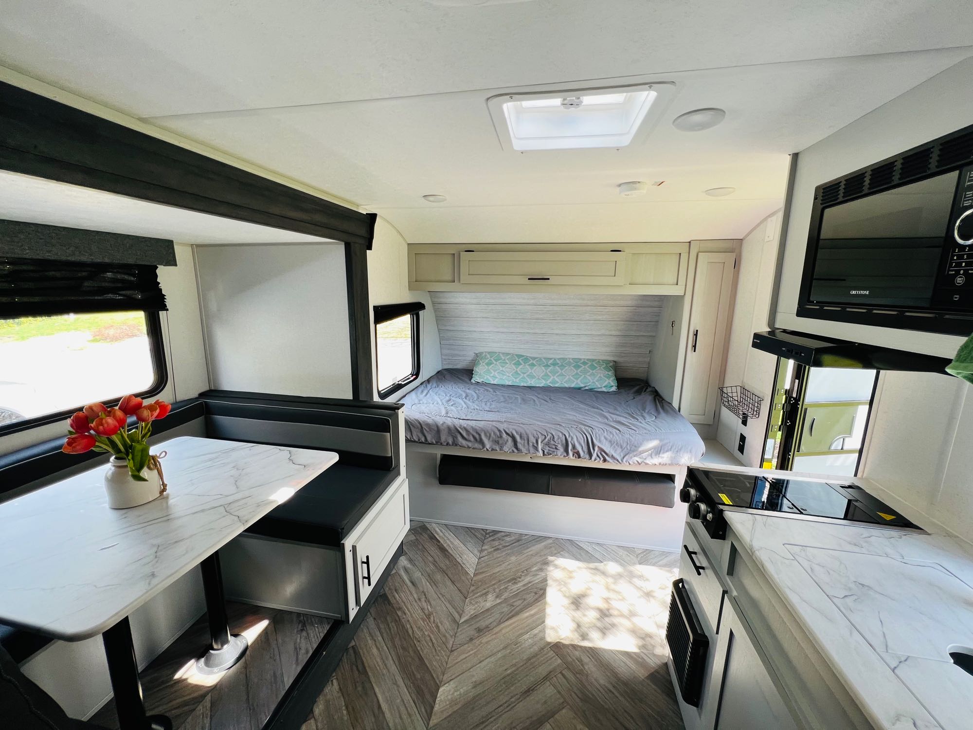Bright, modern rv rental interior showcasing a dining booth, comfortable bed, kitchen, and light wood flooring.. Forest River Wildwood 2022