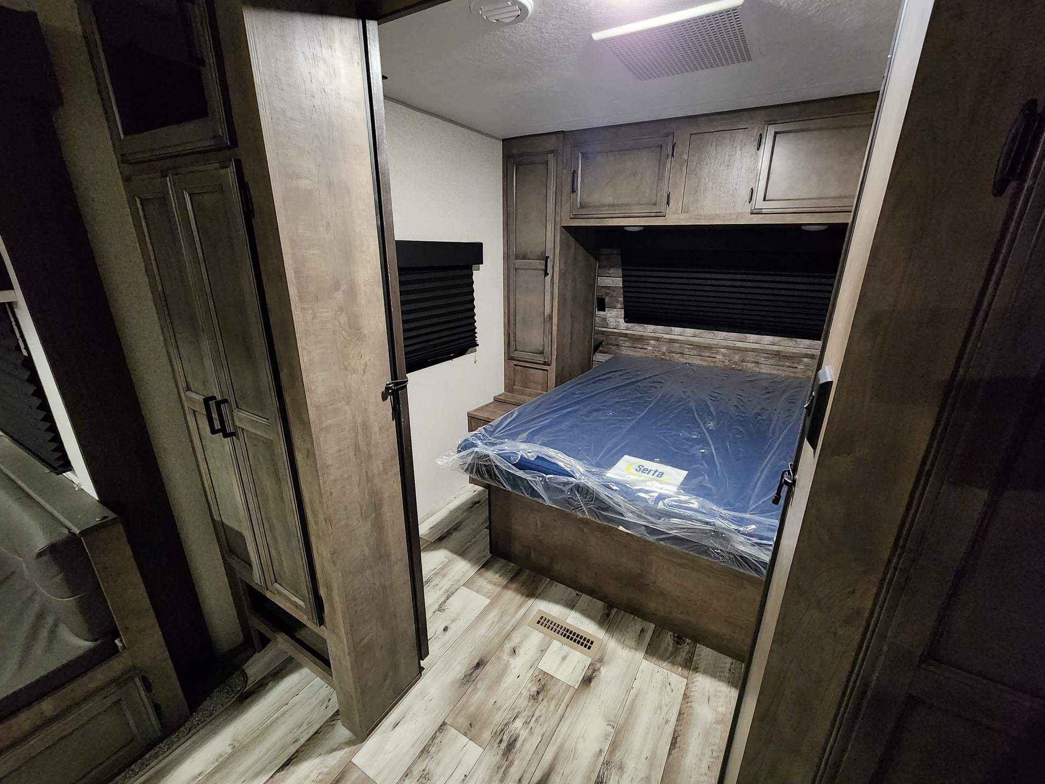 Inside an RV rental: a cozy bedroom with a new Serta bed, built-in cabinets, and wood-look flooring.. Venture Sporttrek 2022