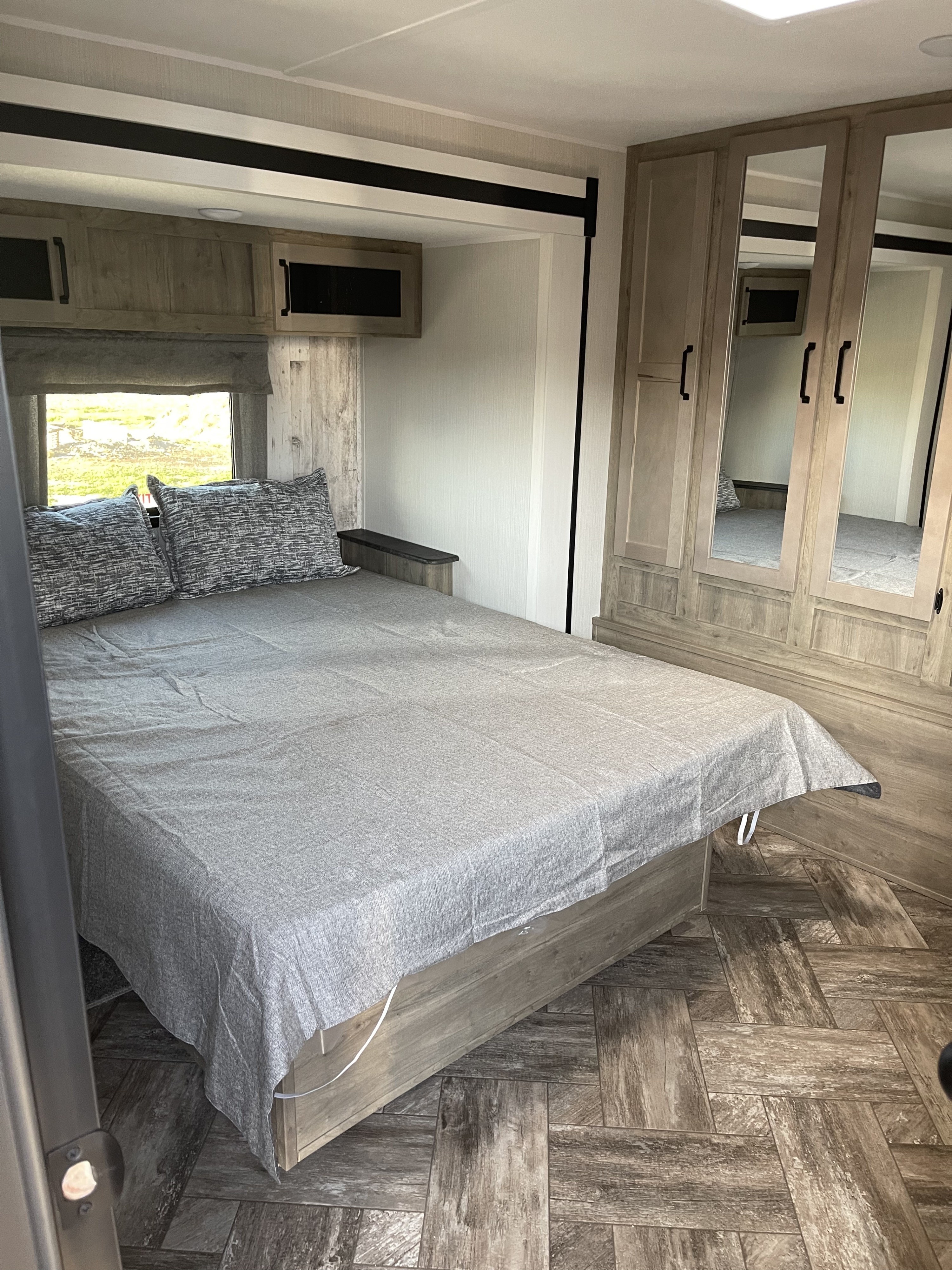 Inside an RV rental: a compact bedroom featuring a comfortable bed, overhead cabinets, and mirrored closet.. Forest River Puma 2023