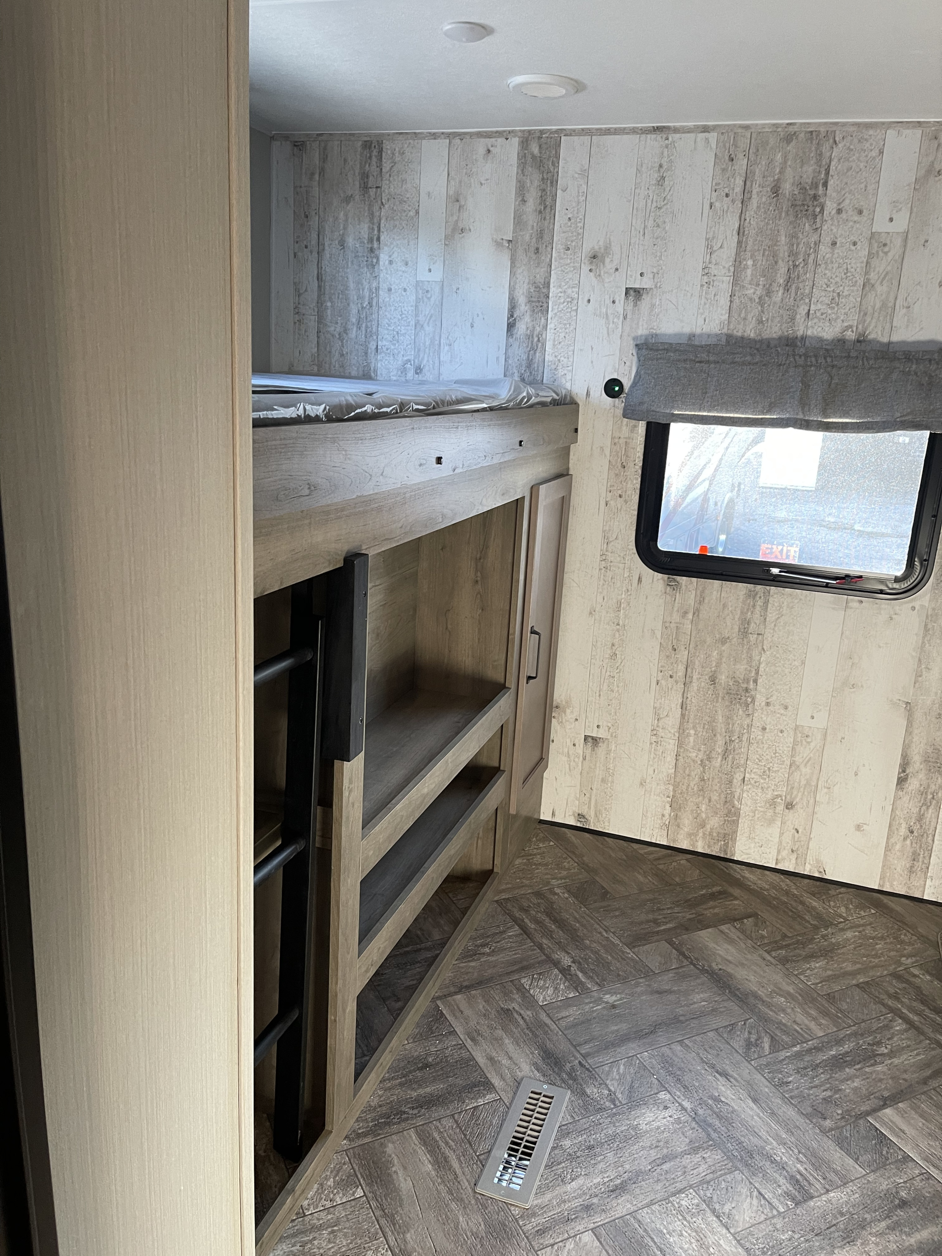 Explore this RV rental's bunk beds, built-in shelves, rustic wood-paneled walls, and unique herringbone floor design.. Forest River Puma 2023