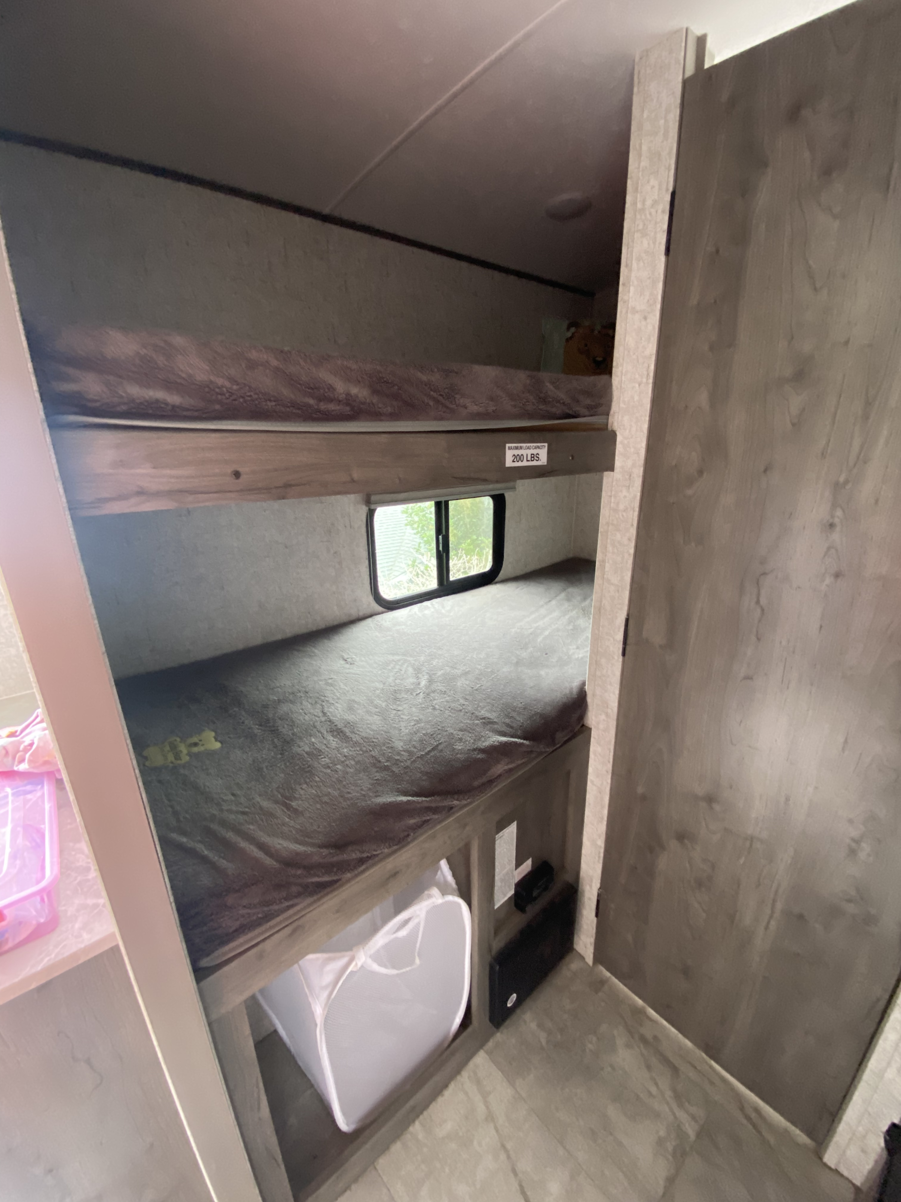 Compact bunk beds in an RV rental, with a 200lb capacity top bunk, window, and laundry hamper storage.. Apex Tera 15T 2020