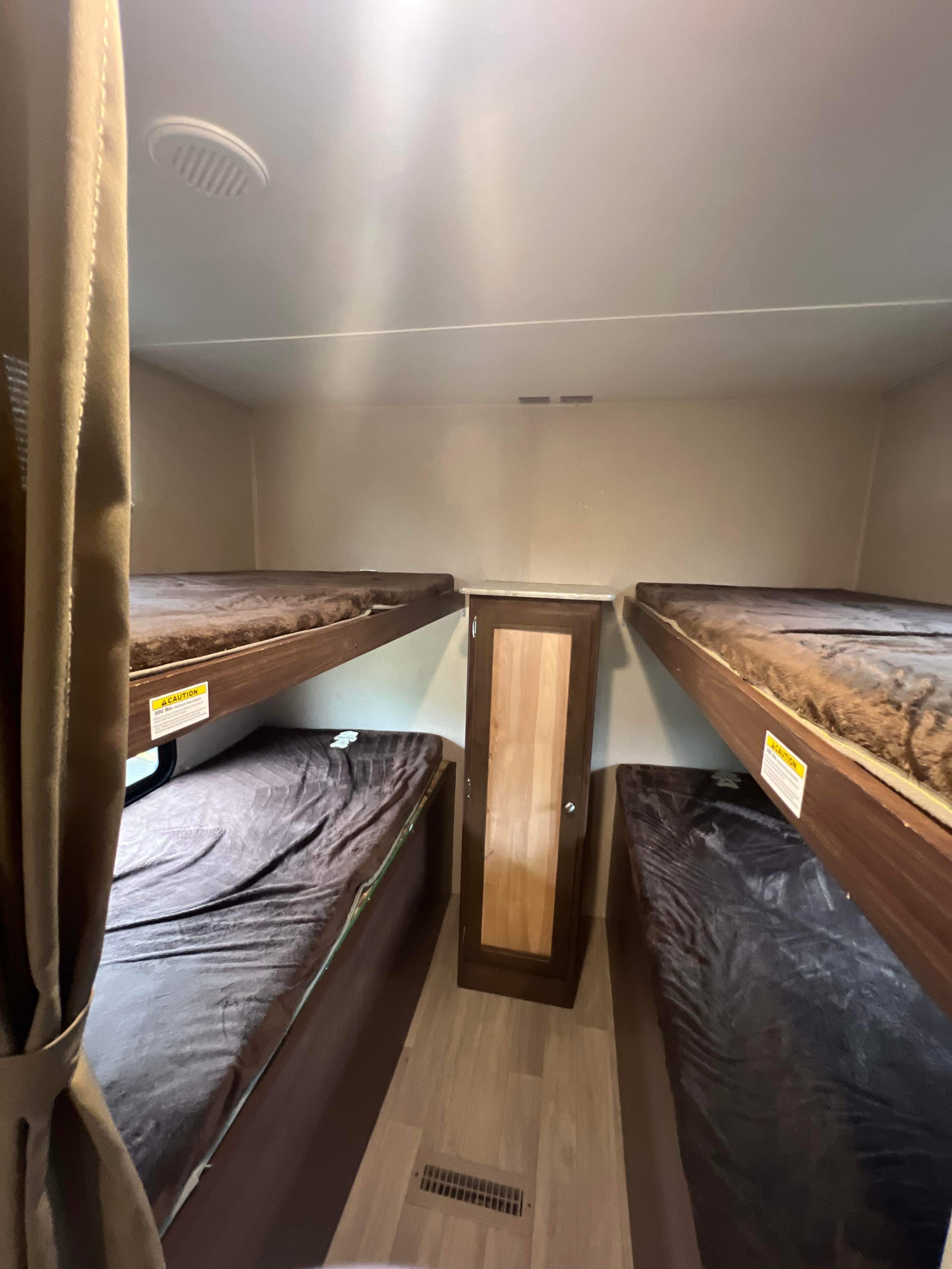 Compact RV rental sleeping area featuring four dark-covered bunk beds, a central cabinet, and a curtain.. Dutchmen Coleman 2018