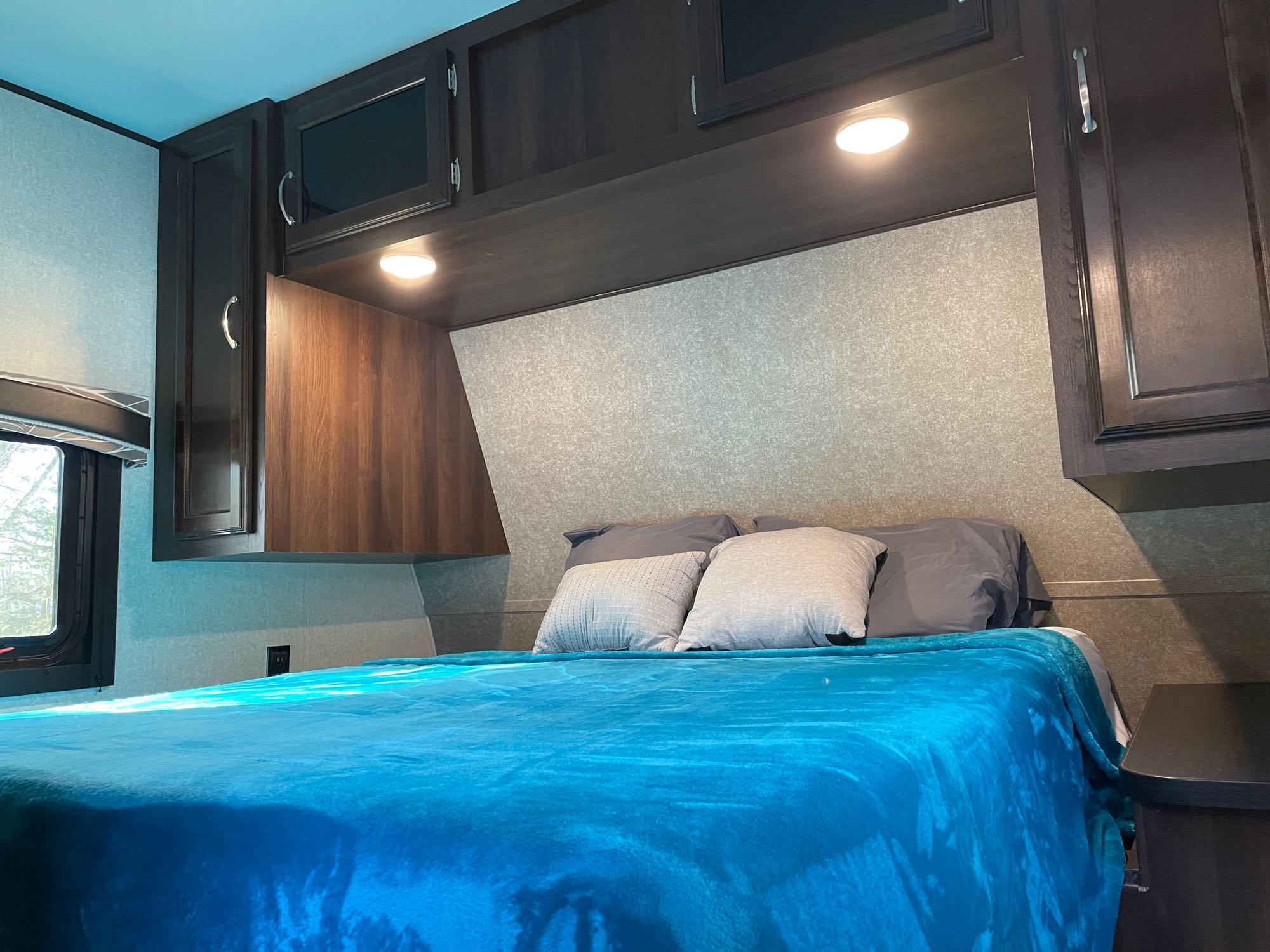 Inside an RV rental, this comfortable bedroom features a full bed with a blue blanket, overhead cabinets, and reading lights.. Jayco Jay Flight 2018