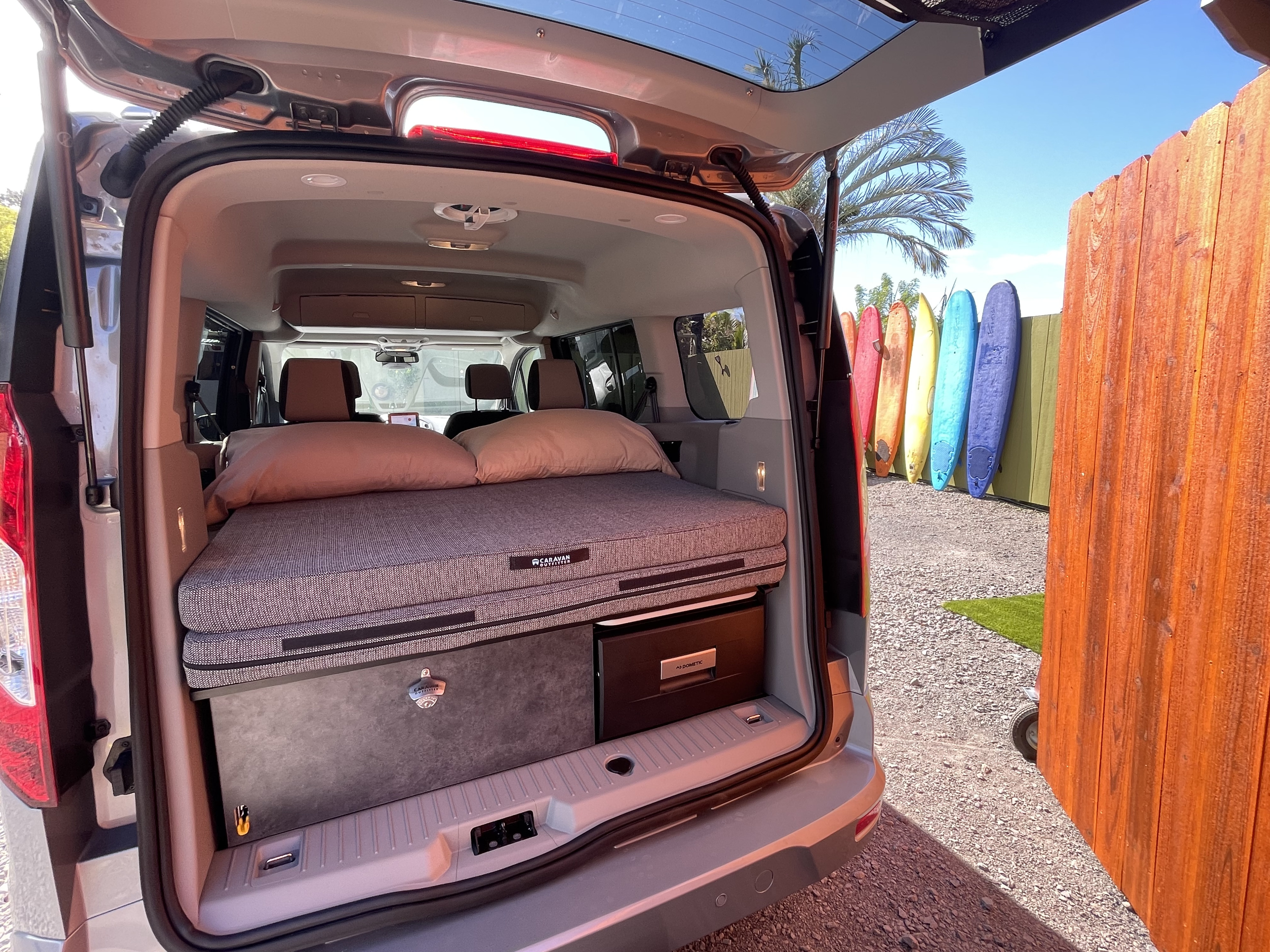 Compact camper van RV rental setup with cozy bed, storage, and fridge, perfect for surf adventures!. Ford Transit Connect Wagon 2022