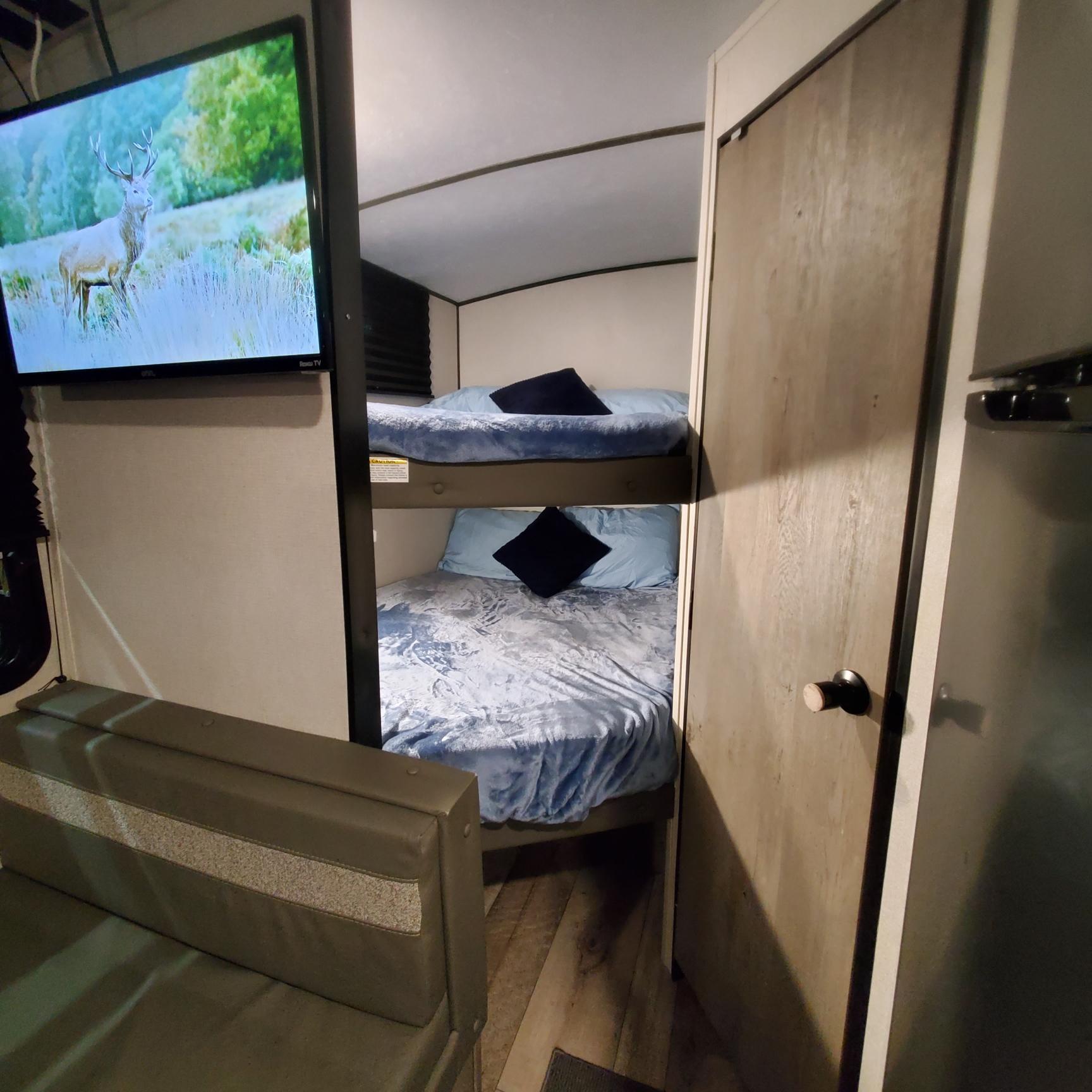 Cozy RV rental interior: bunk beds with blue bedding, comfy couch, and a TV showing a deer. Great for family trips!. Keystone RV Springdale 2021