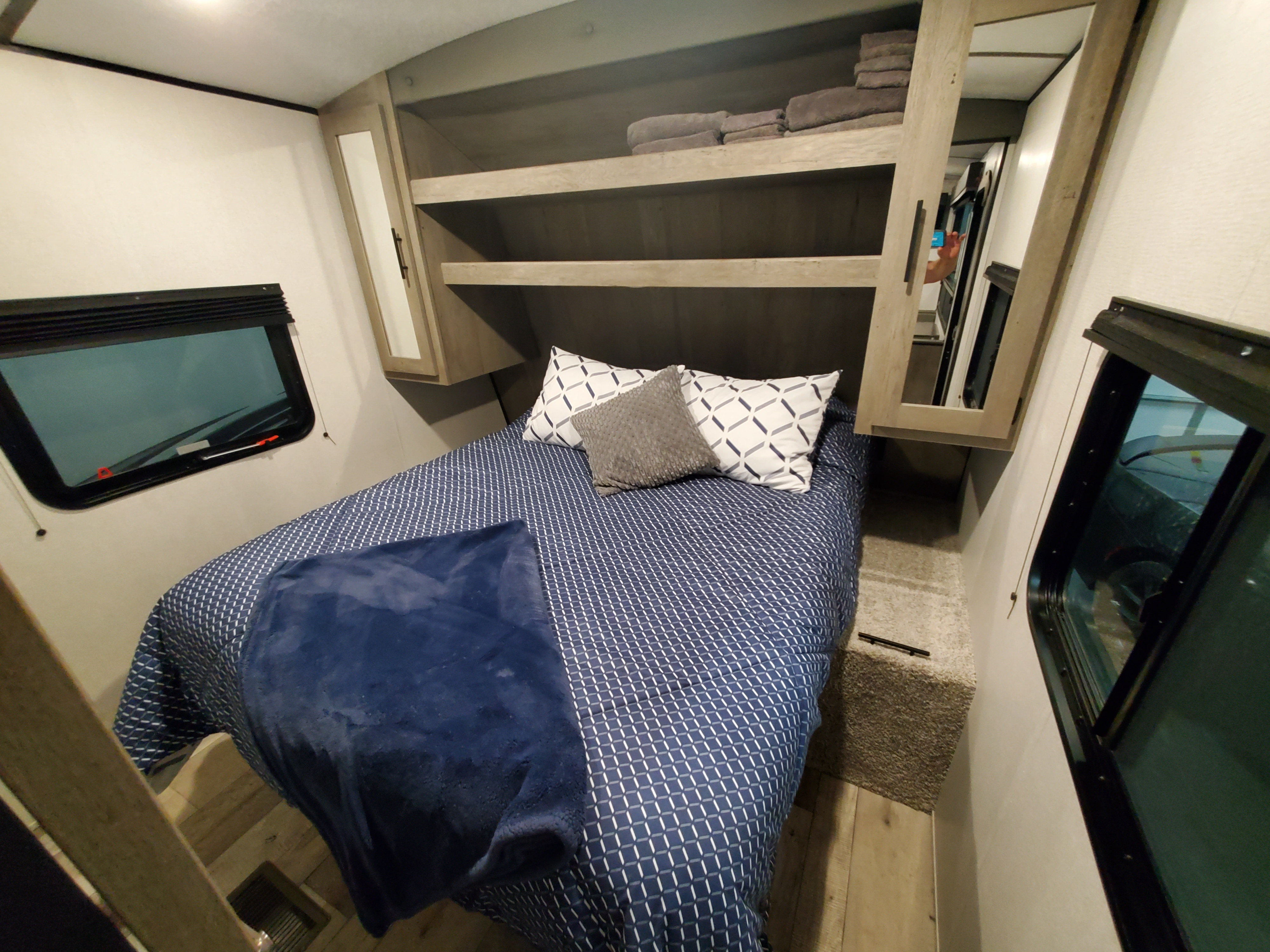 This RV rental's cozy bedroom features a patterned bed, dark blue blanket, and overhead storage. Ready for your trip!. Keystone RV Springdale 2021