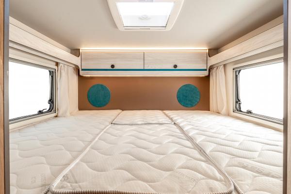 RV rental bedroom interior: A spacious bed with light mattress, side windows, overhead cabinets, and accent lights.. Rimor Kilig 95 Plus 2023