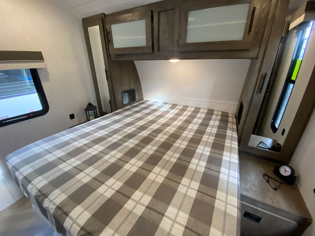 Cozy RV rental bedroom featuring a plaid bedspread, overhead storage, and a side window for a comfortable travel experience.. Forest River Wildwood 2021
