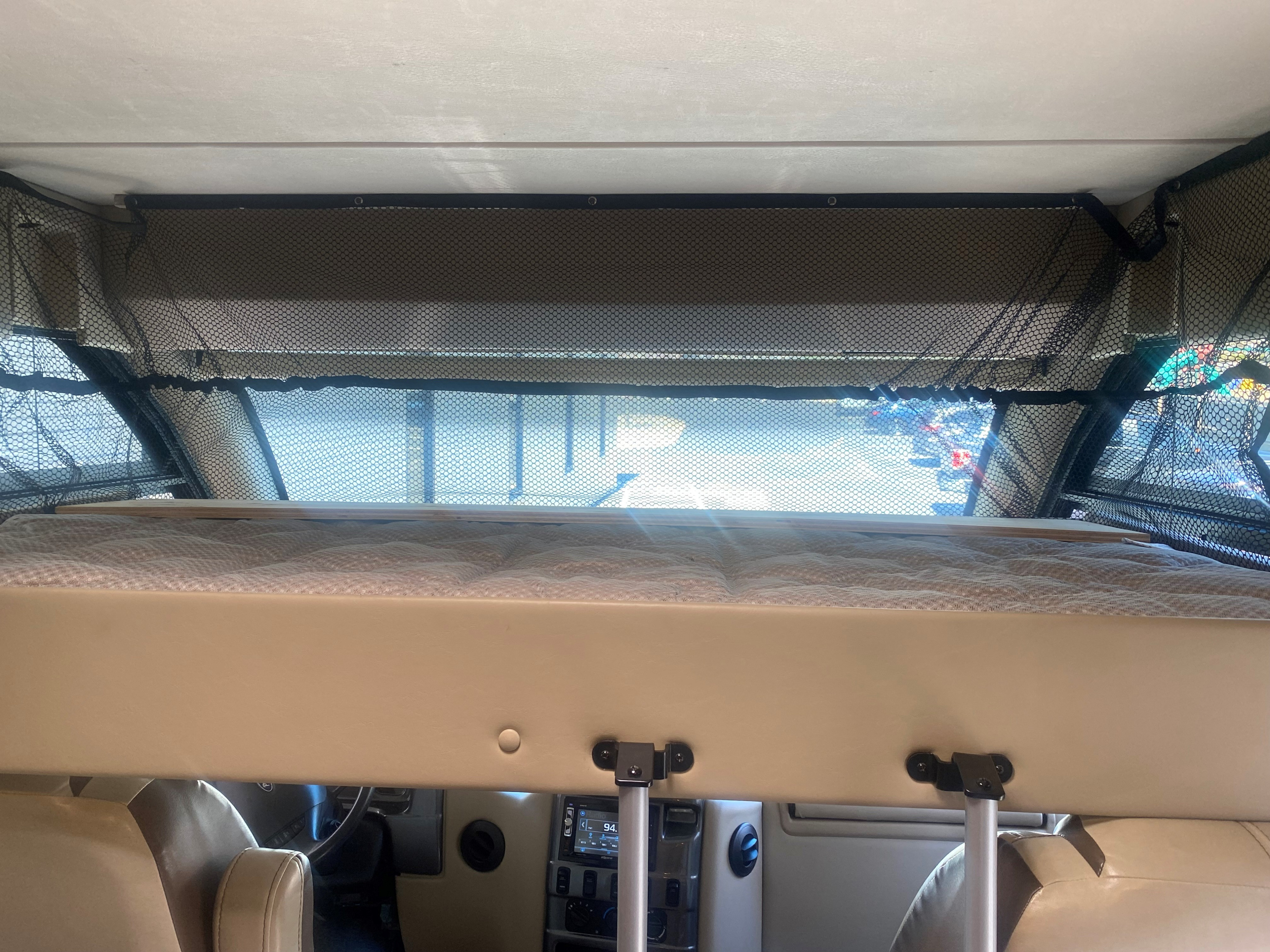 Overhead bunk bed with safety net in an RV rental, showing the driver's cabin below.. Thor Vegas 2018