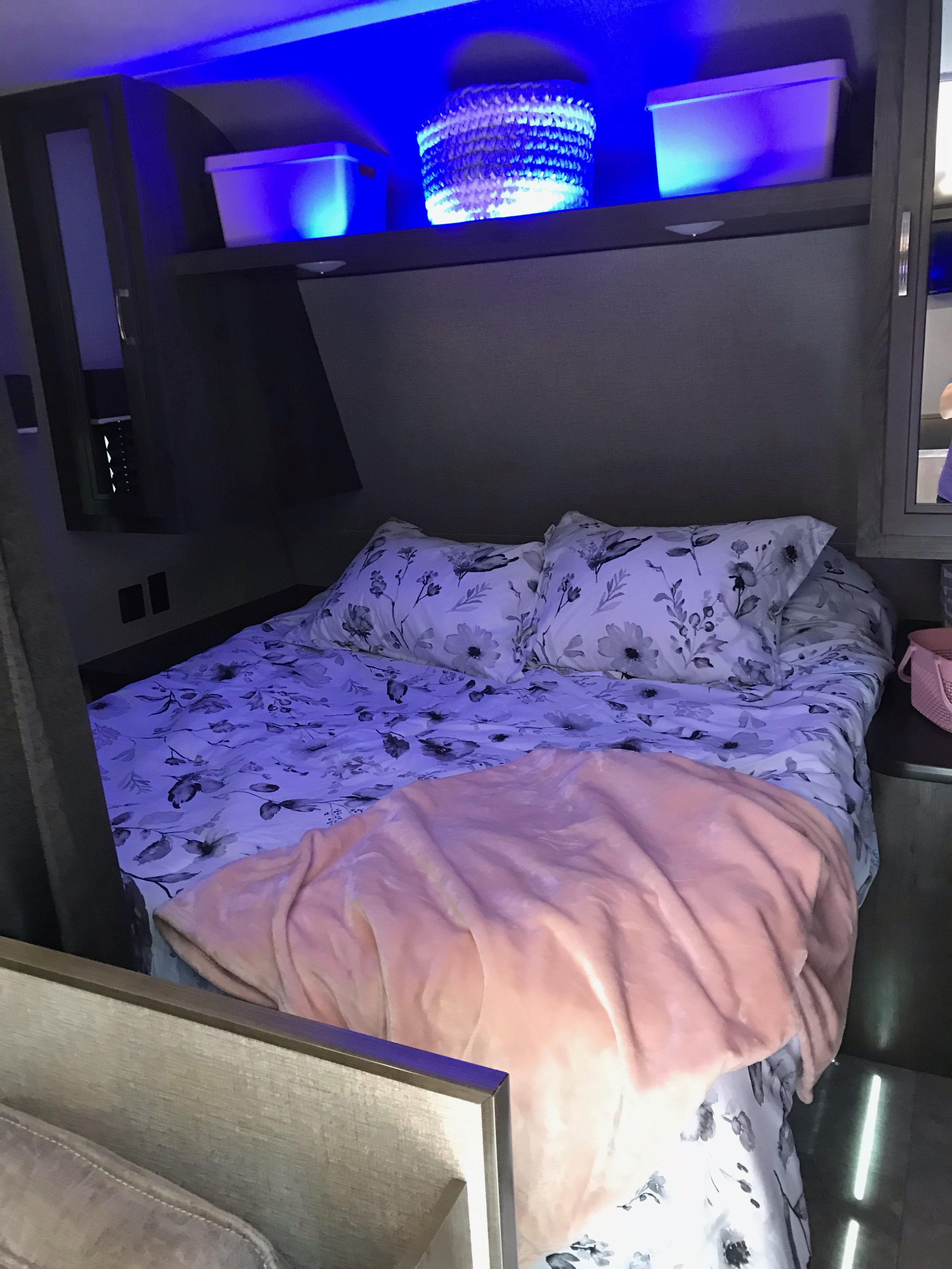 Cozy RV rental bedroom with floral bedding, a soft pink blanket, and blue-lit shelf storage above the bed.. Jayco Jay Flight SLX 2020