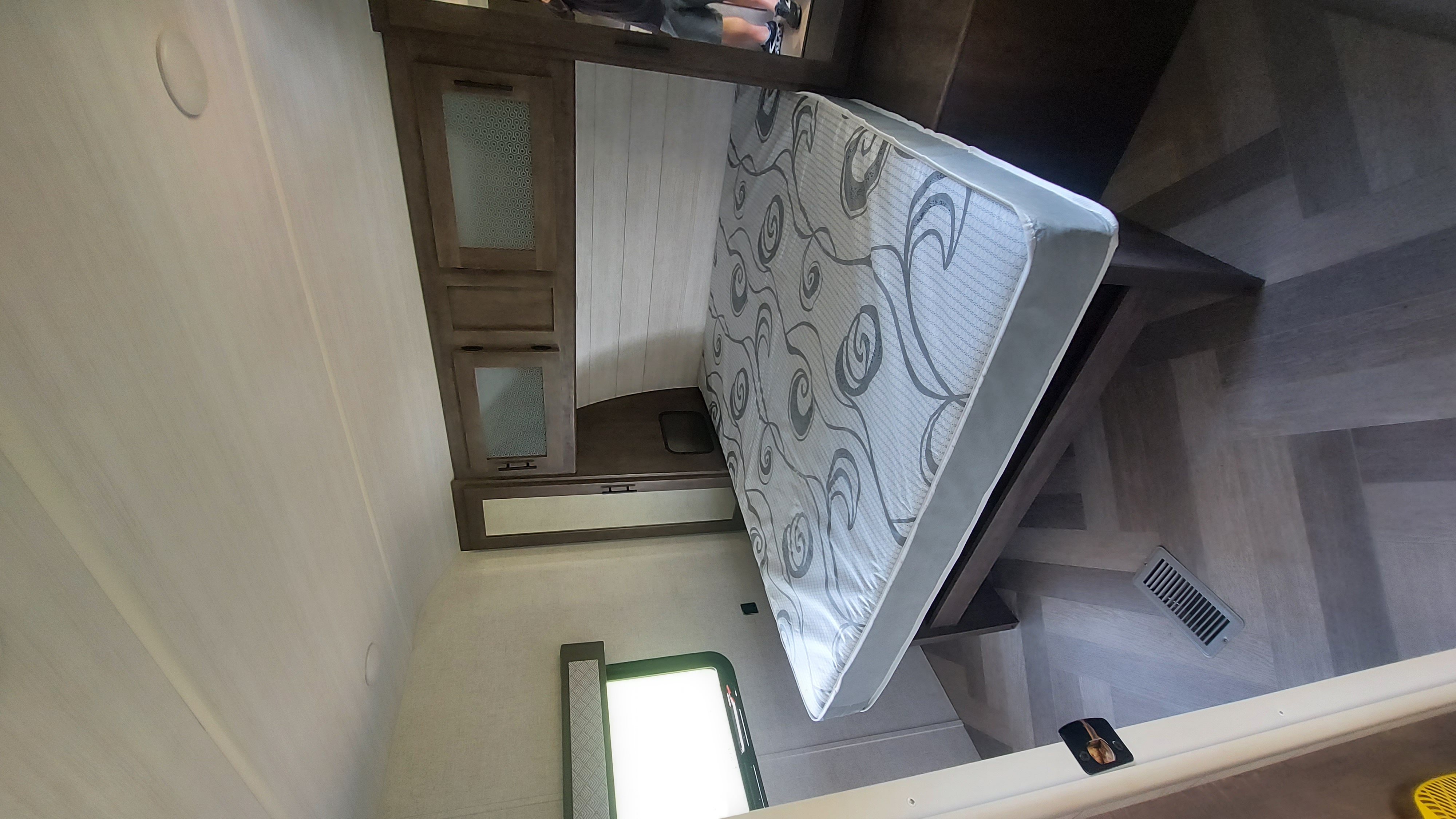 Explore this RV rental's compact bedroom with a patterned mattress, dark wood cabinets, and modern flooring.. Forest River Wildwood 2020